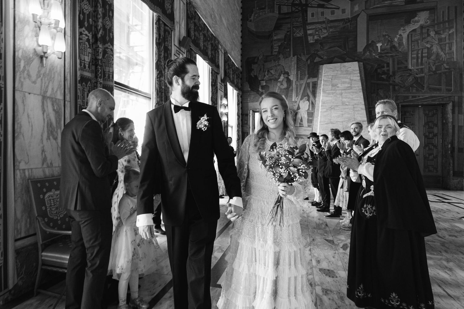 Wedding party gathering in an ornate hall with painted murals and natural light.