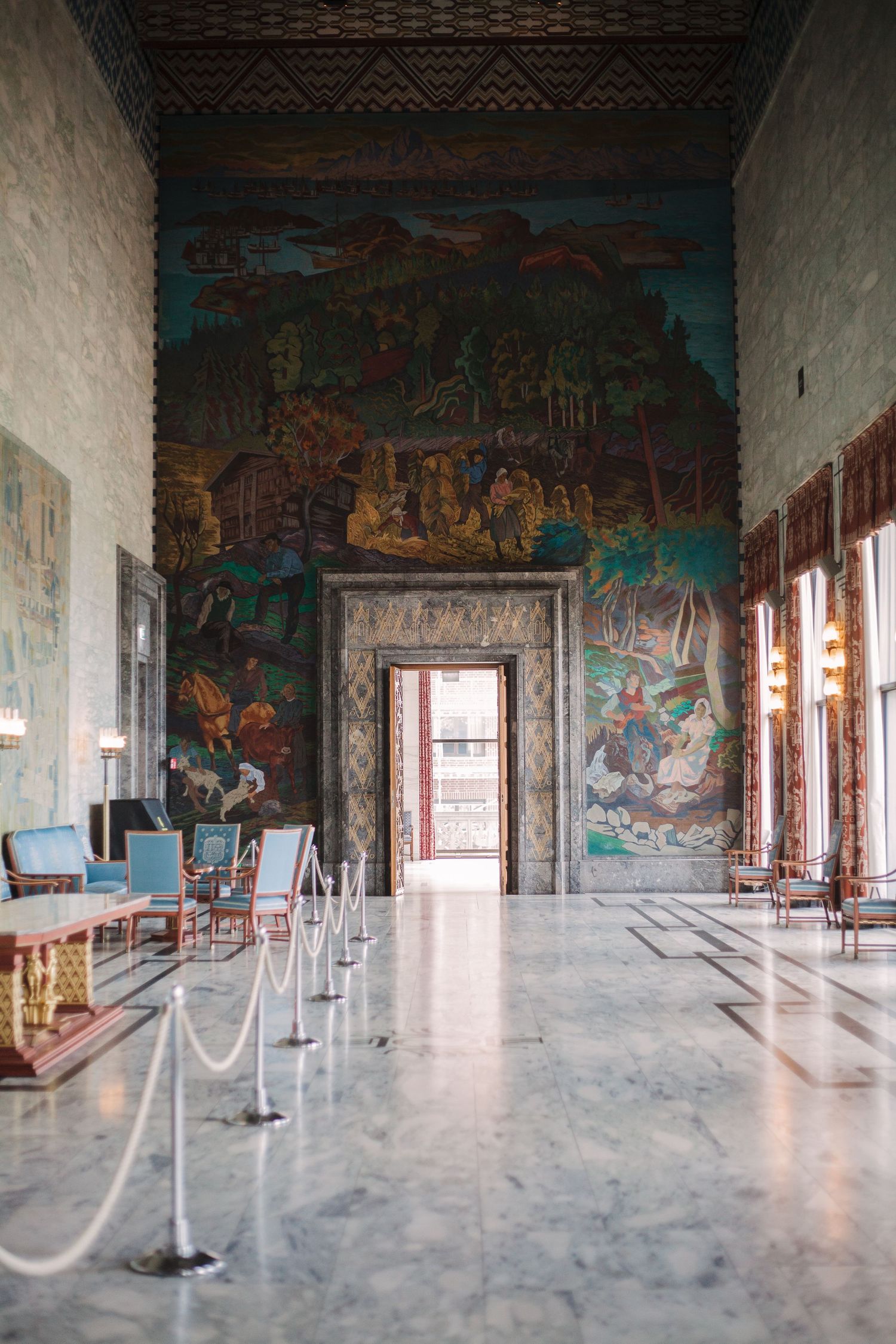 Grand hall with colorful murals on walls and marble floors with rope barriers.