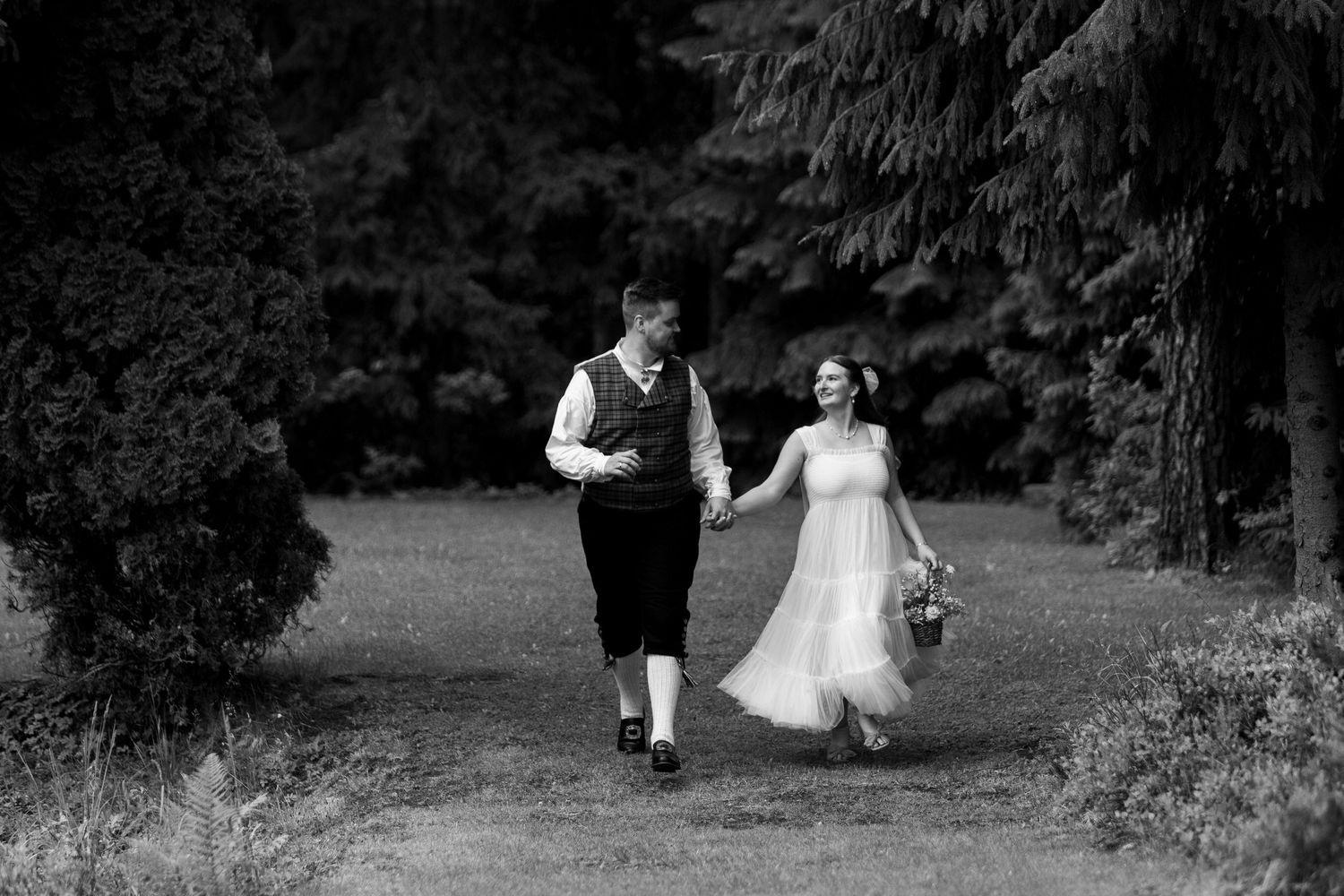 Black and white wedding photography capturing a couple walking through a wooded area.