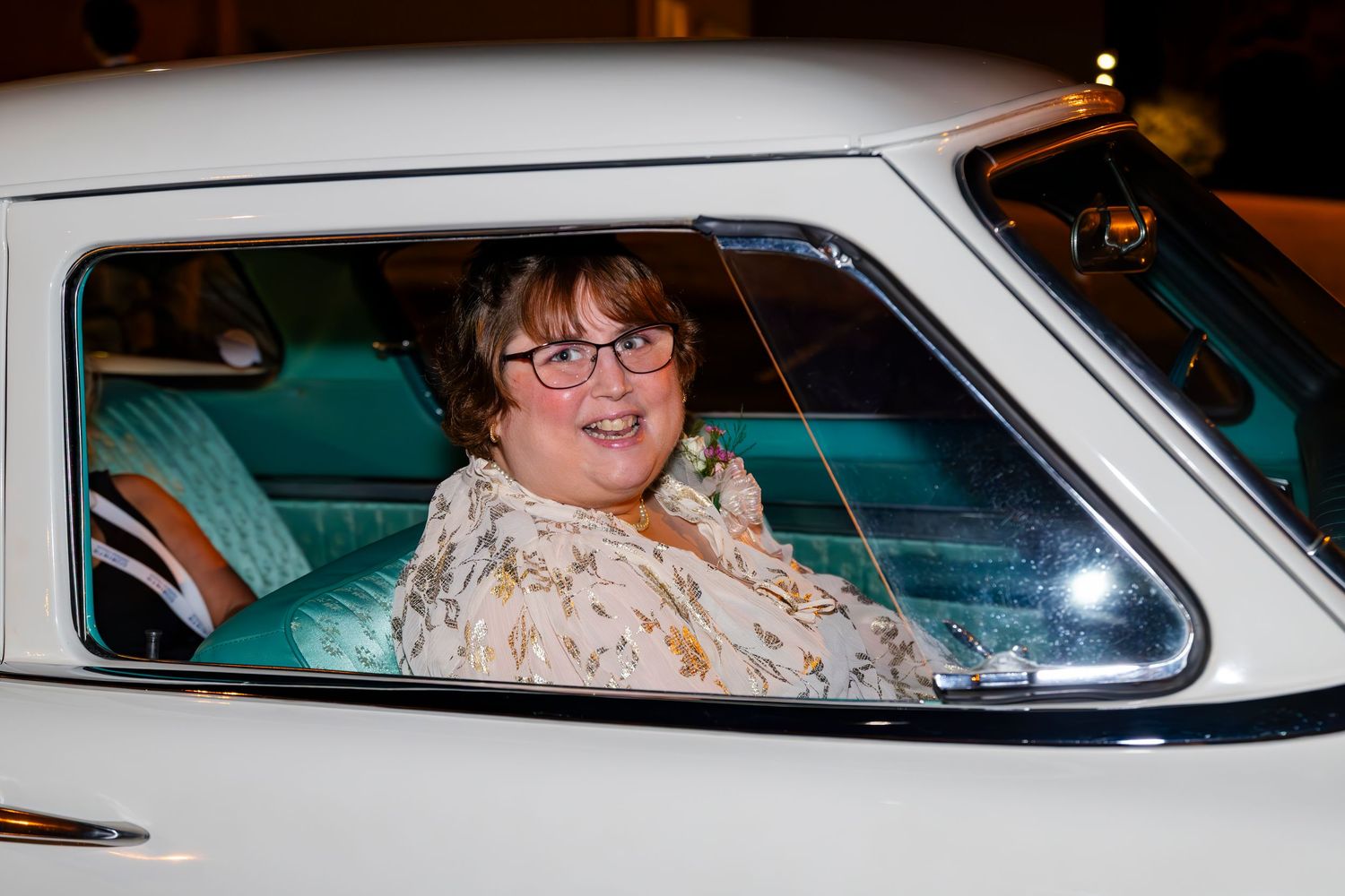 Person sitting in vintage car at night smiling through driver's side window.