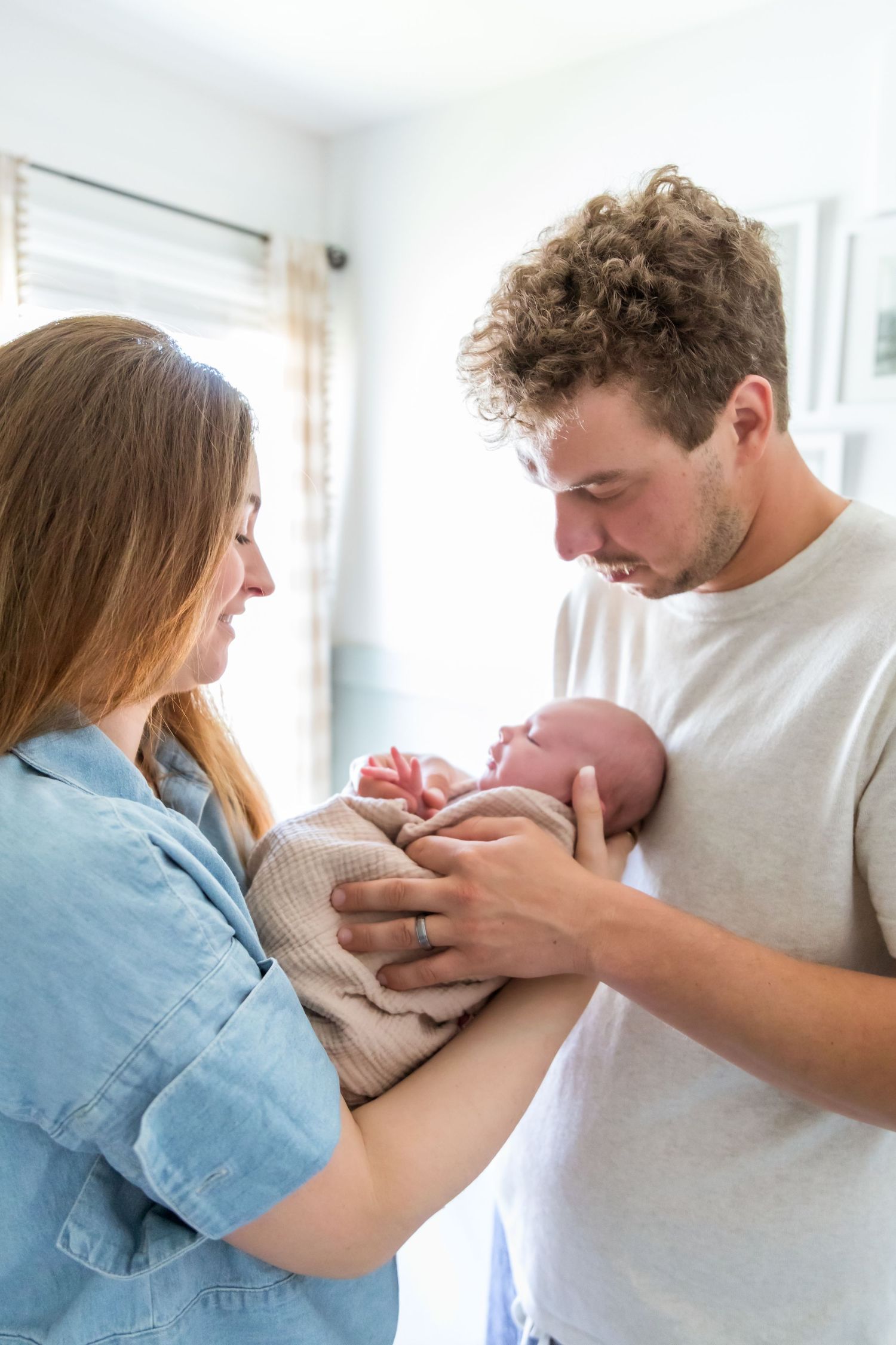 New parents hold their newborn baby together in a bright, warmly lit room.