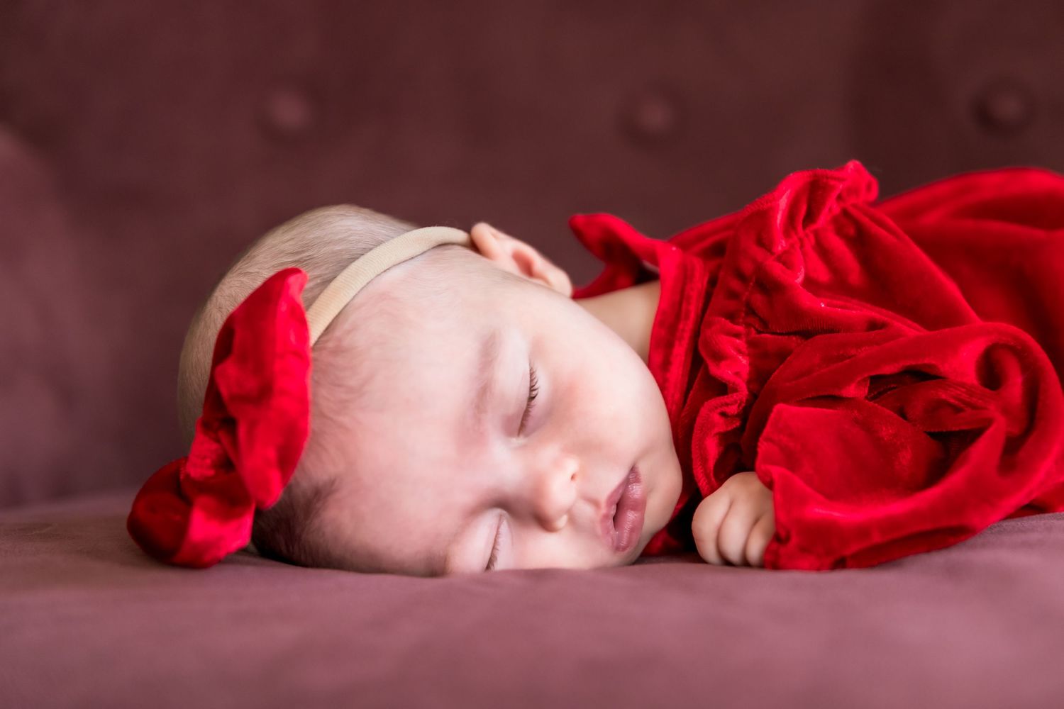 Sleeping newborn wrapped in soft red fabric against dark background.