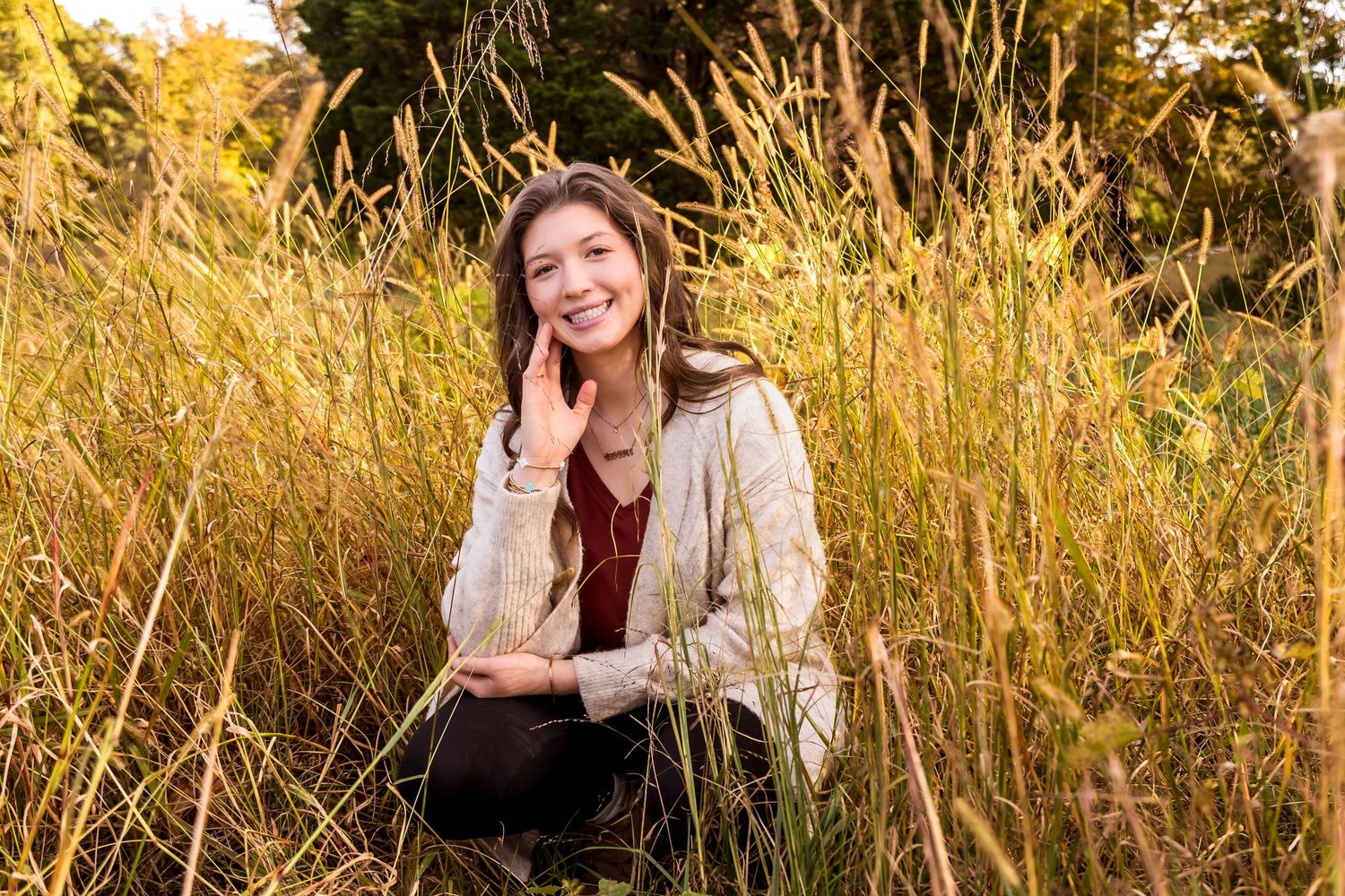 Woman sitting in golden field of tall grass during sunset.