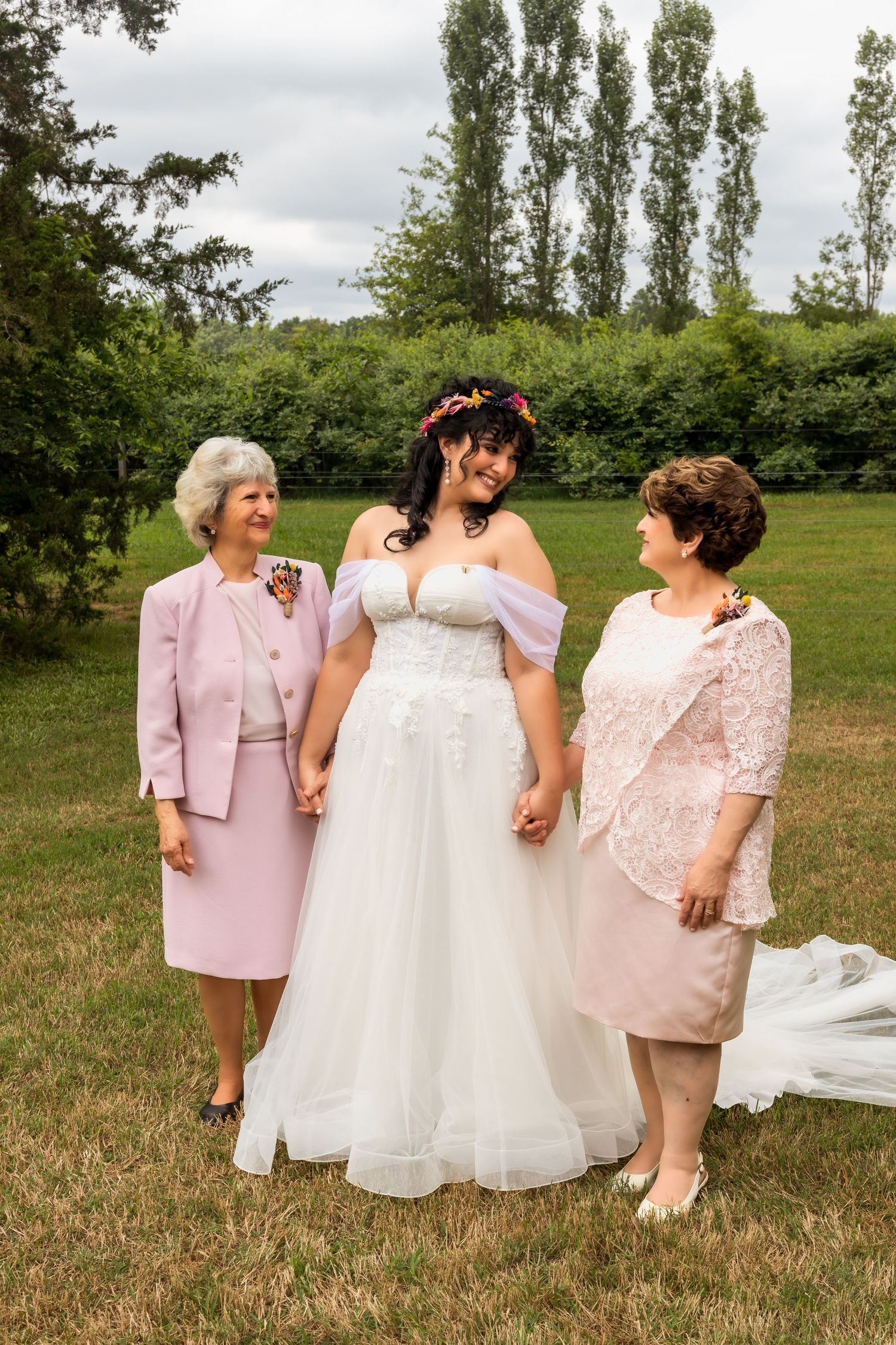 Wedding party in pink and white attire poses casually on grassy field.