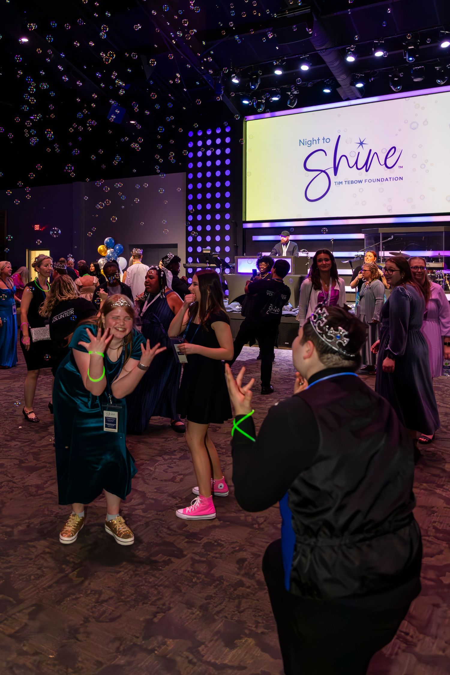 Dance party with colorful lighting and people dancing on a dark carpeted floor.