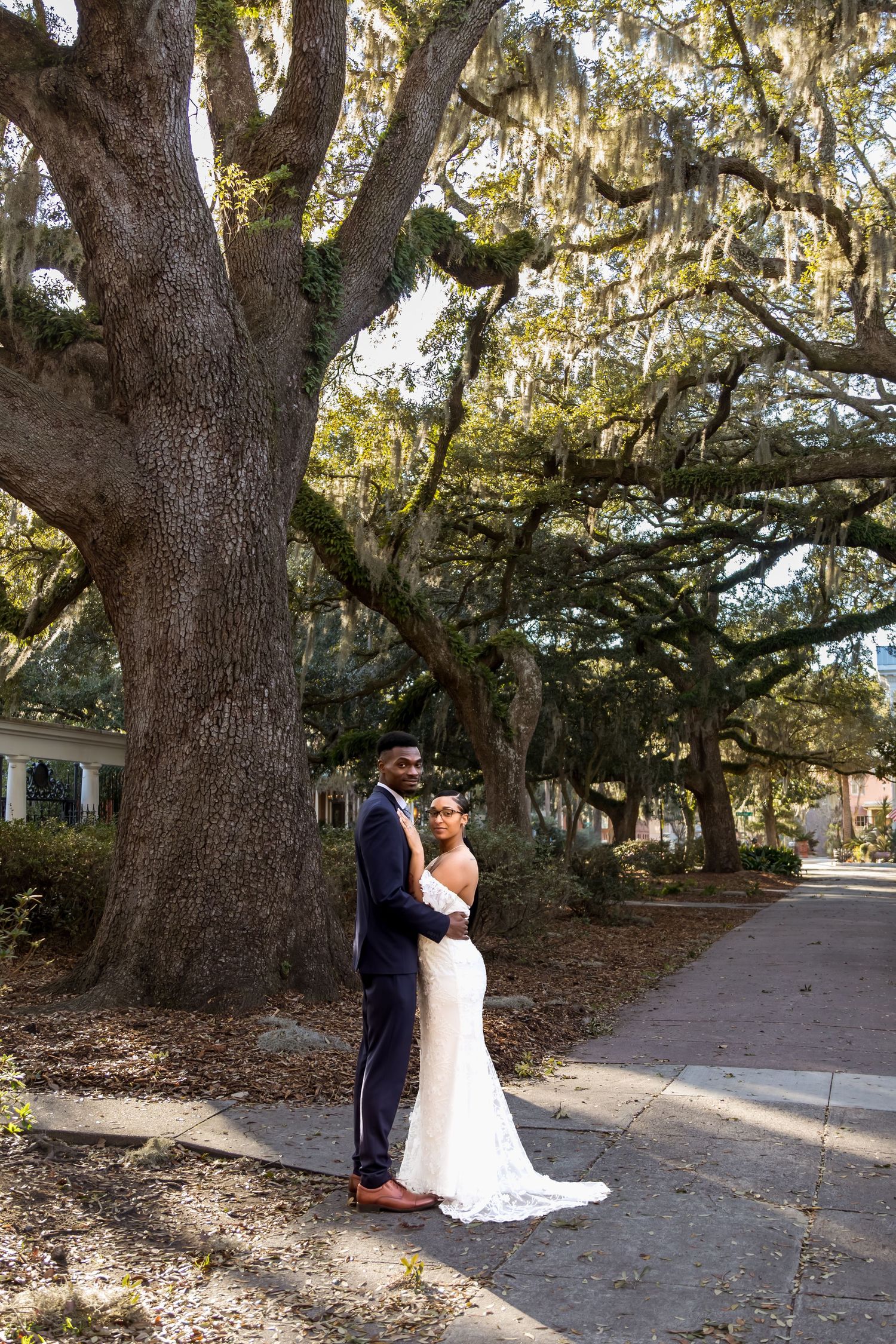 A romantic couple shares an intimate moment beneath majestic oak trees draped in Spanish moss on a winding path.