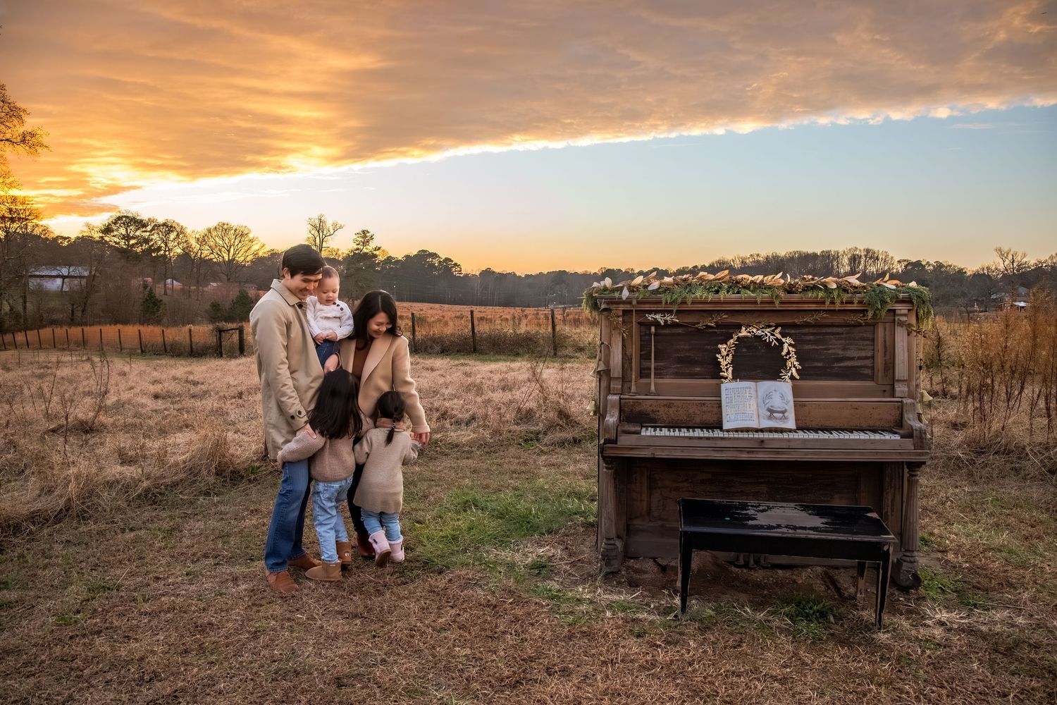 A couple stands near a vintage piano in a rustic field during a golden sunset.
