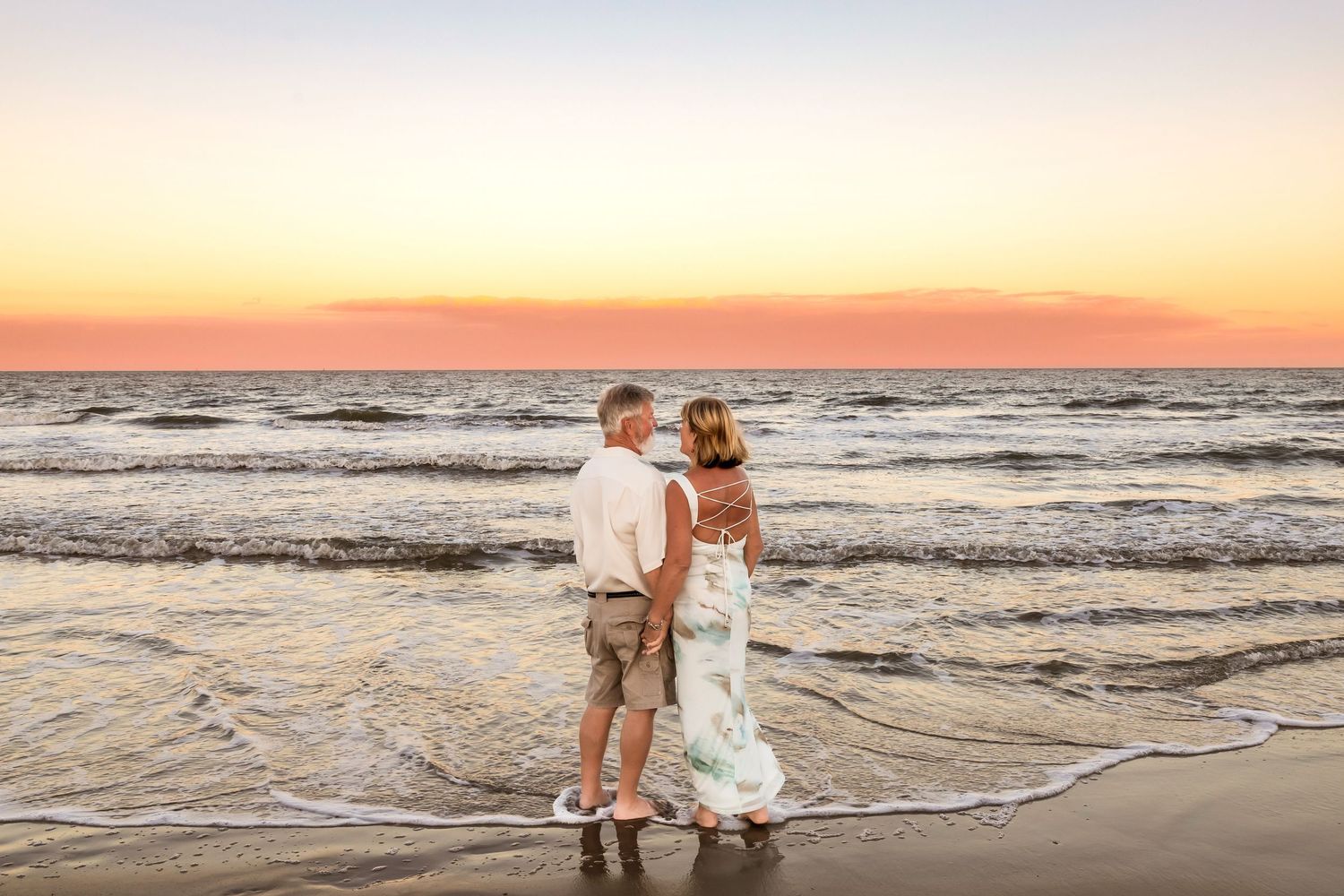 A couple stands together at the beach during a beautiful golden sunset as waves roll onto the shore.