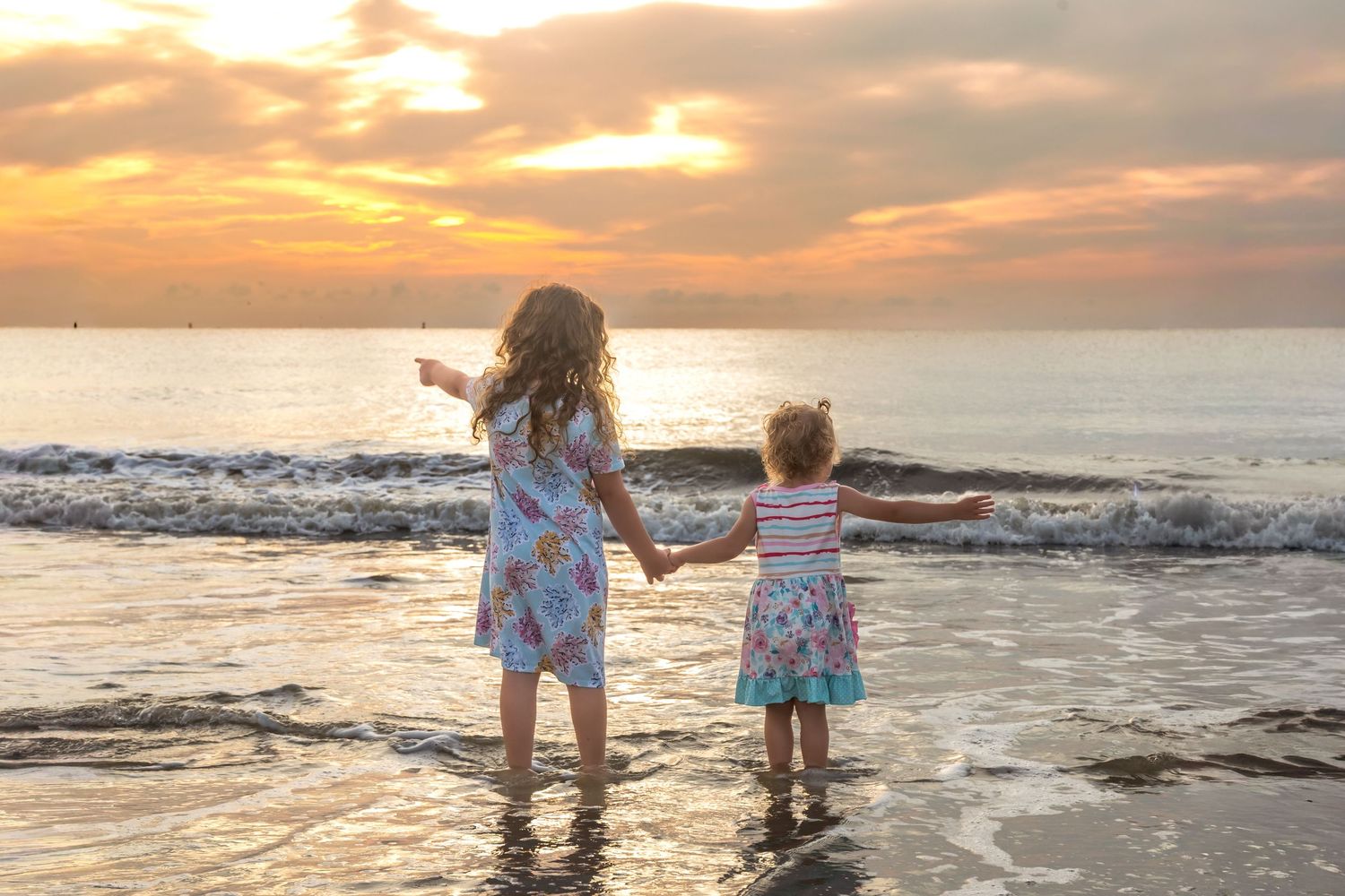 Two children playing in ocean waves during golden sunset.