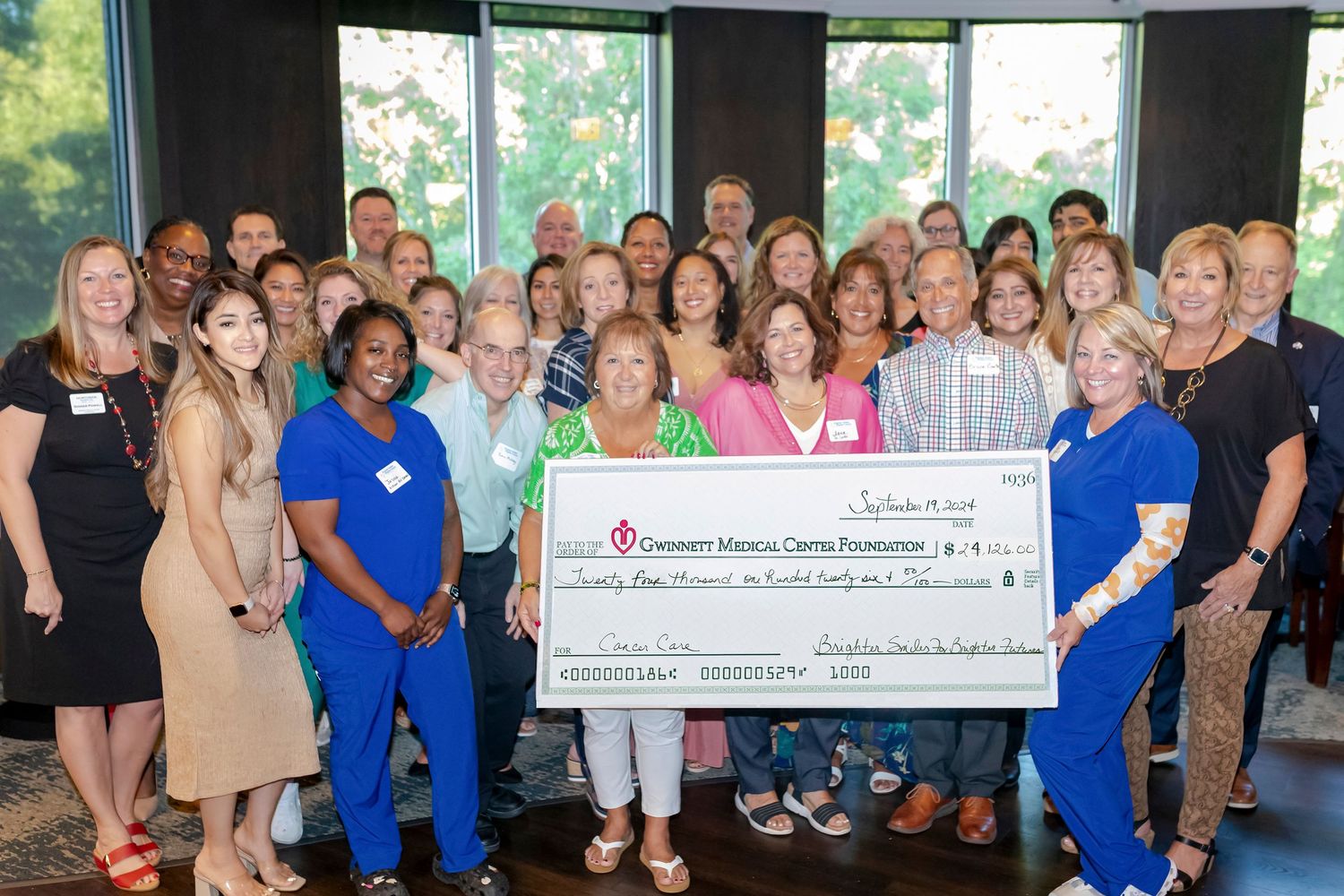 Large group photo with people holding a presentation check at a charity event.