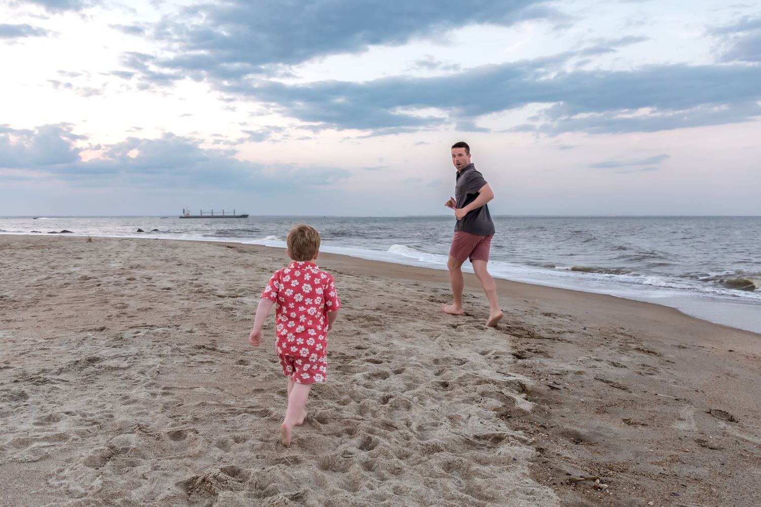 A child and adult playing on a sandy beach at dusk near the ocean shoreline.