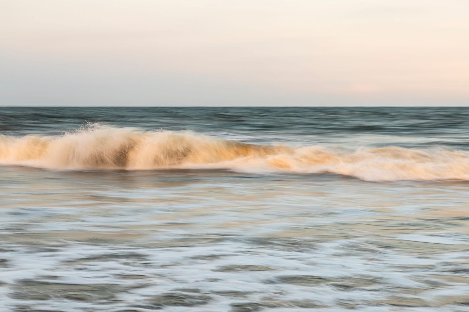 Serene ocean waves breaking at sunset with warm tones.