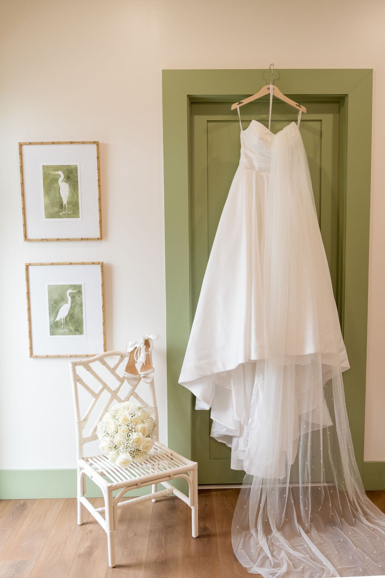 Wedding dress and veil displayed elegantly against white wall with green accents.