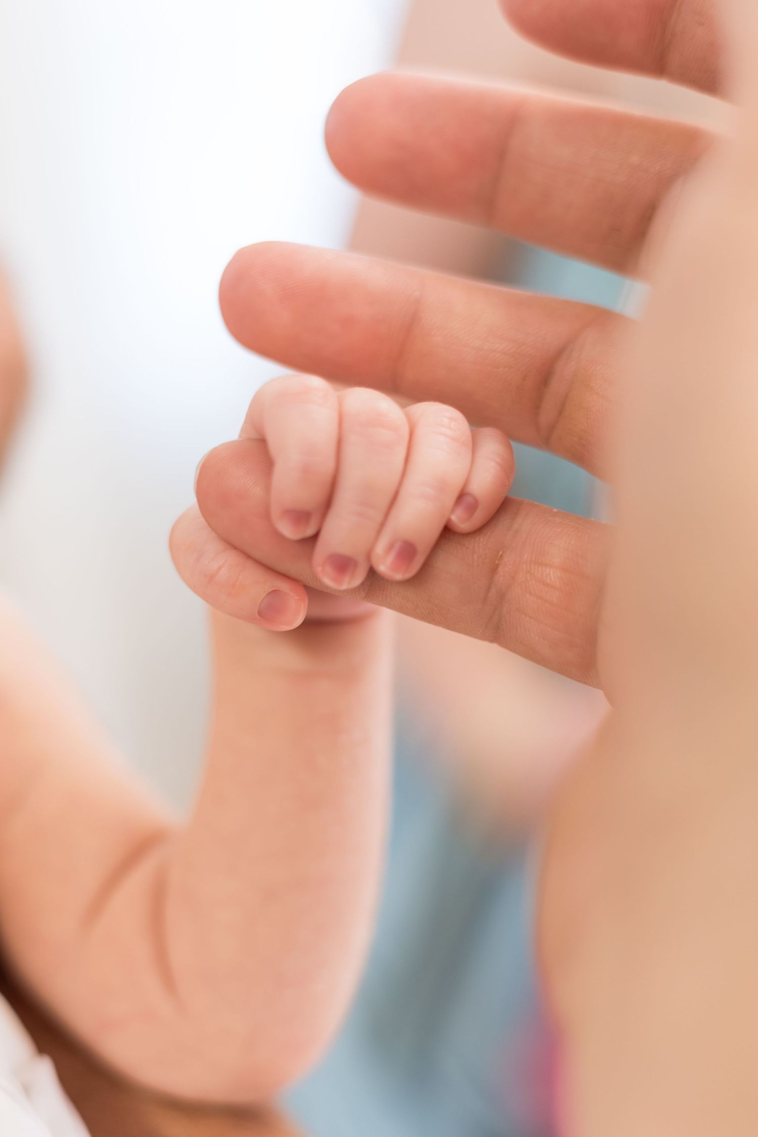 A tiny newborn baby hand gently gripping an adult finger, symbolizing trust and the bond between parent and child.