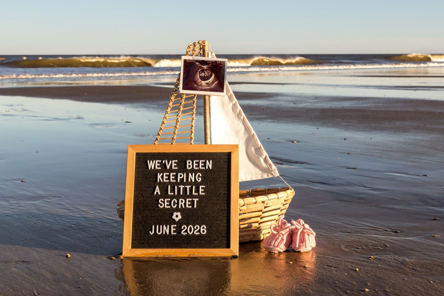 Chalkboard sign with inspirational message stands on sandy beach with ocean waves in background.