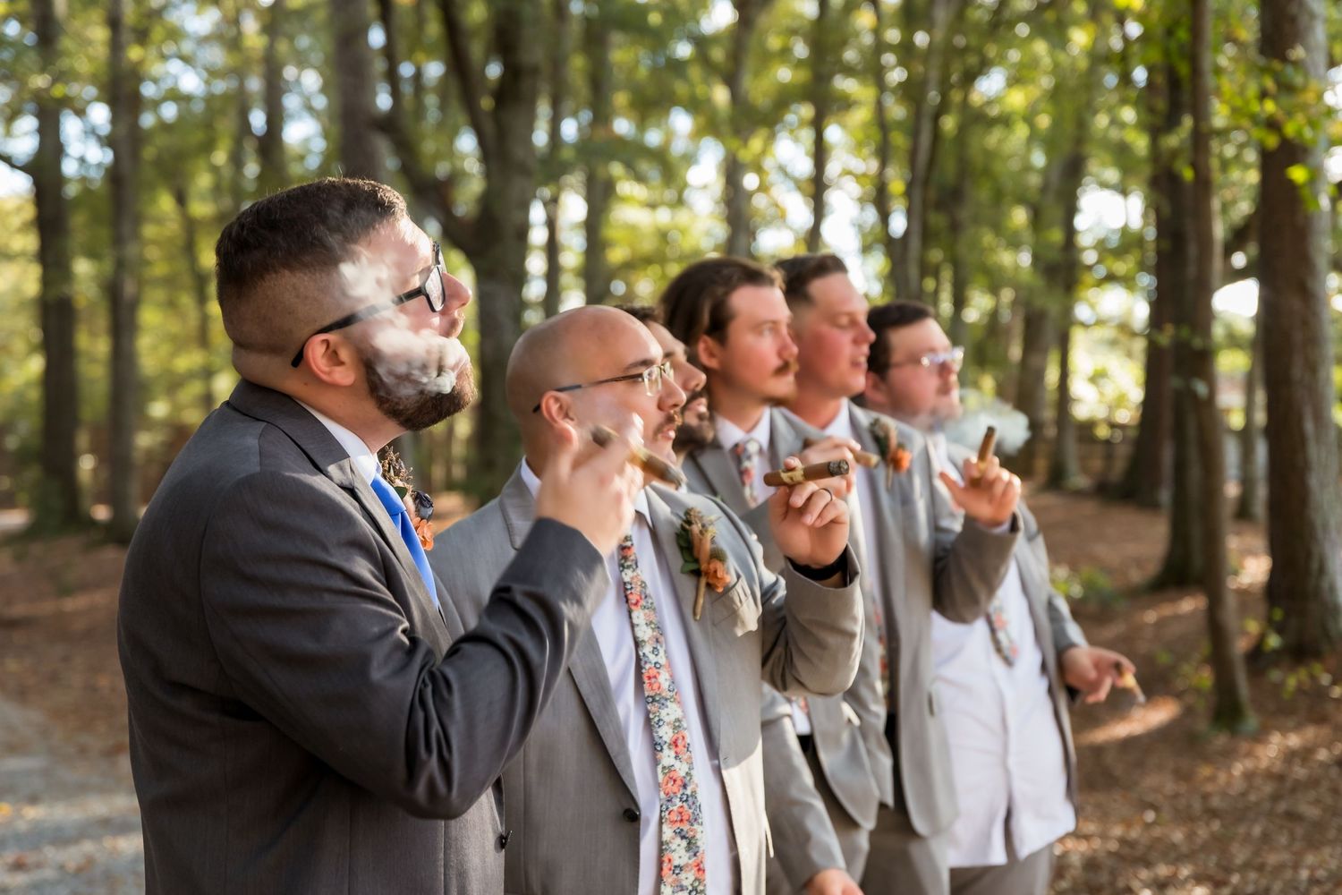 Groomsmen in gray suits pose playfully in a wooded outdoor setting.