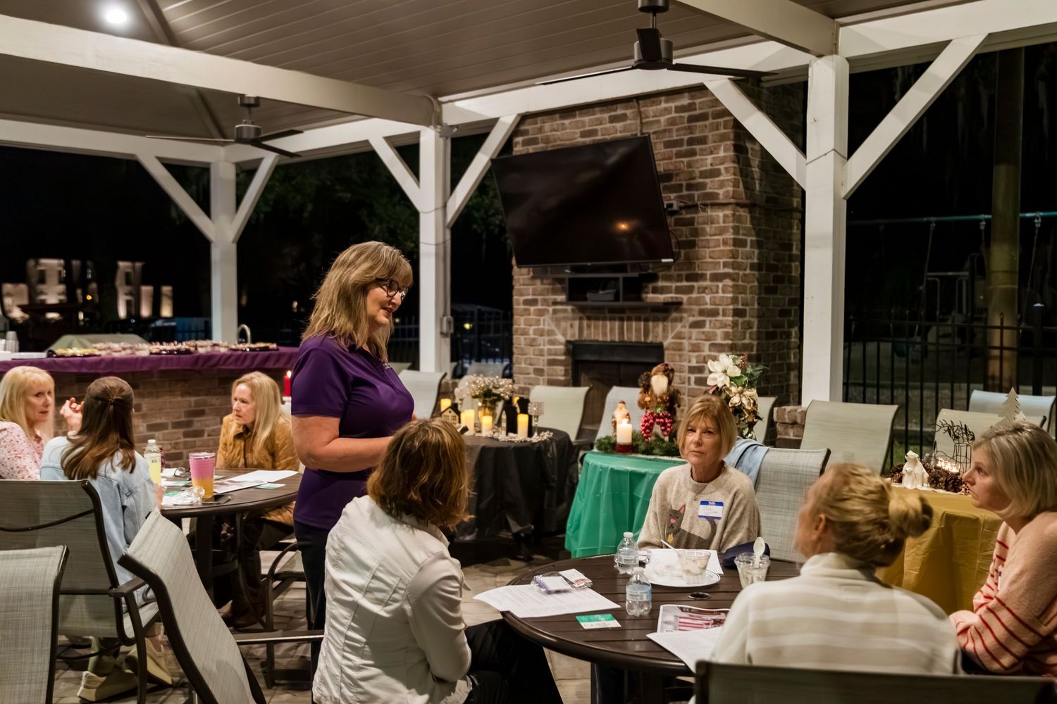 Guests enjoying dinner and conversation on an outdoor covered patio with brick fireplace.