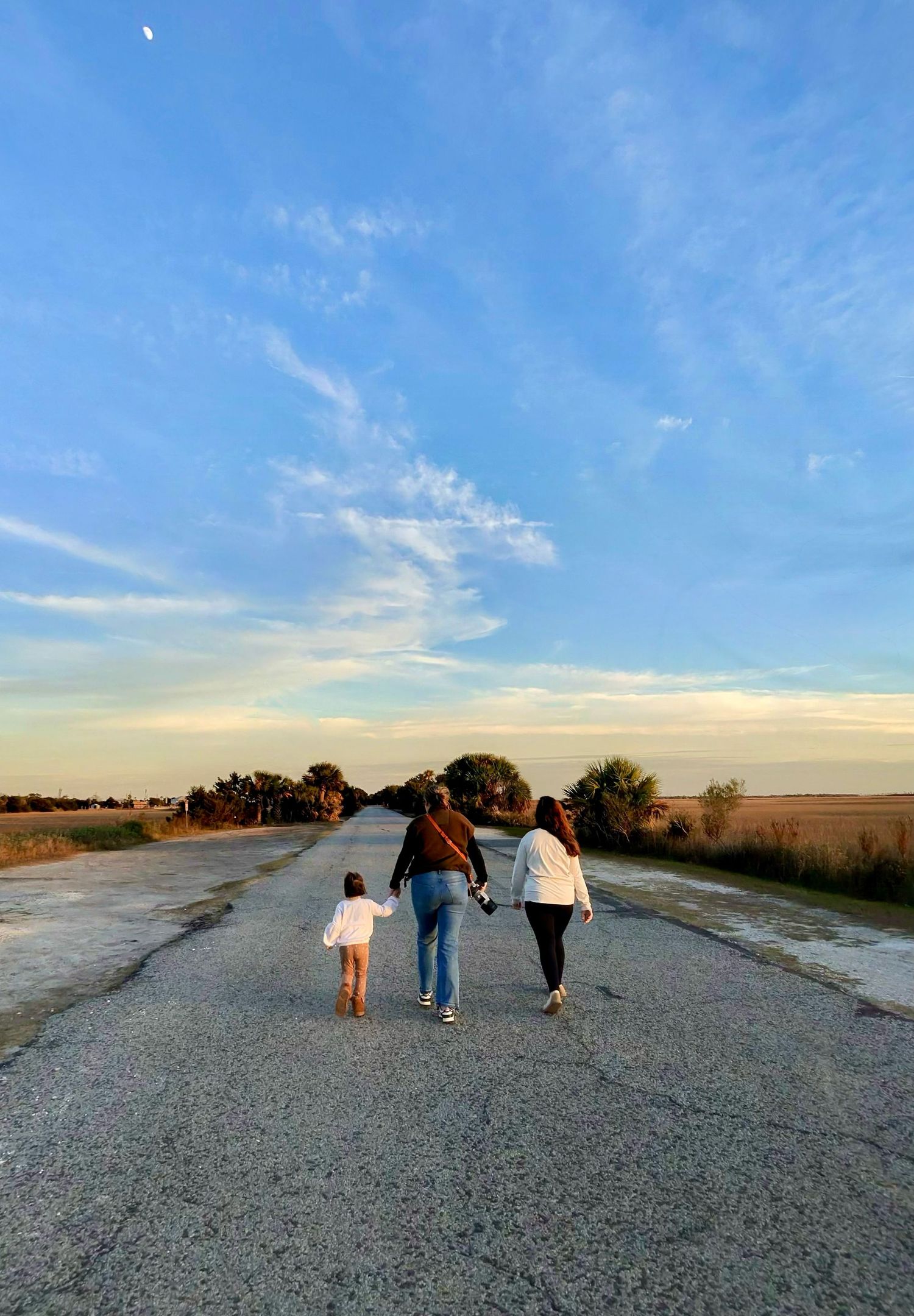Three people walking together down a rural road at sunset with a blue sky and wispy clouds overhead.