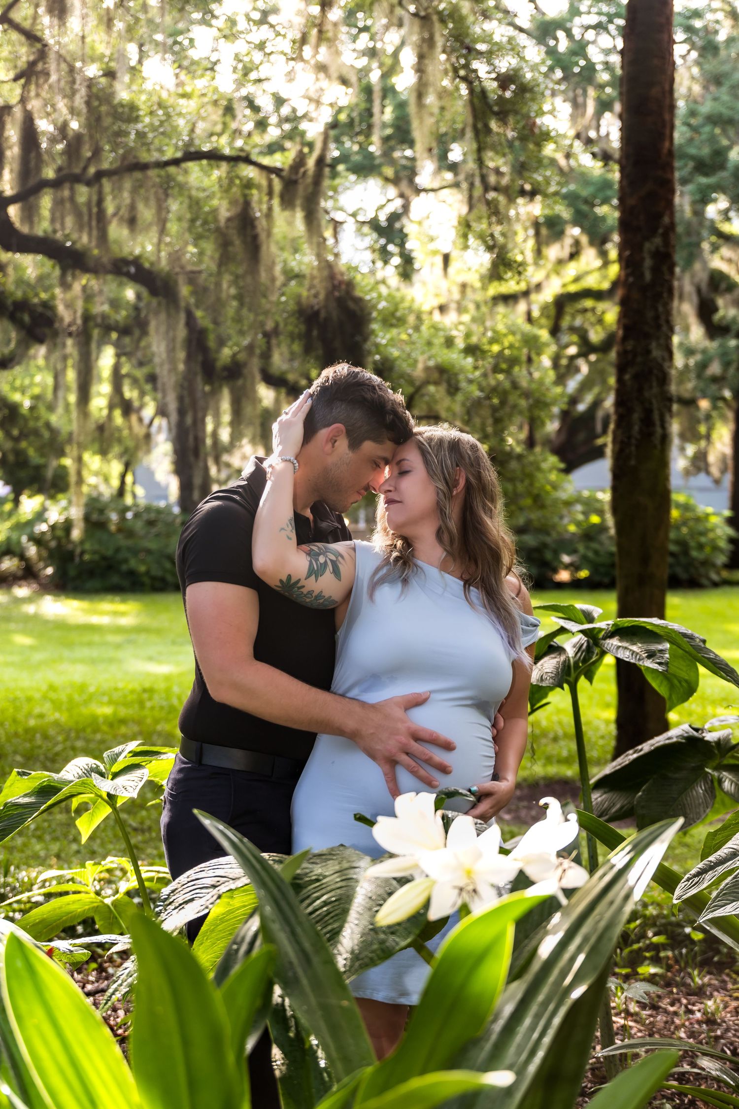Romantic maternity photo in garden with tropical plants and Spanish moss.