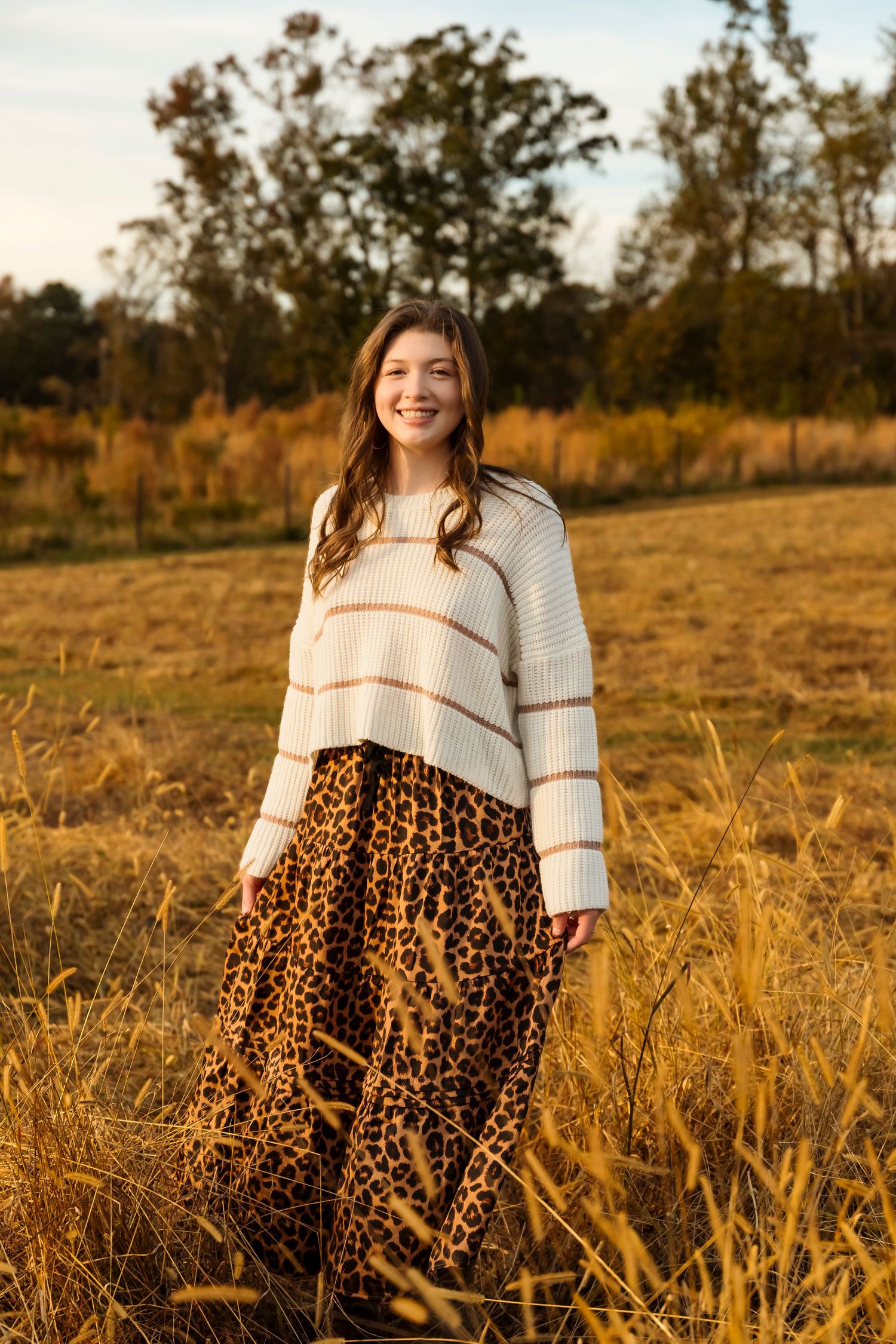 Portrait in cream sweater and leopard print skirt standing in autumn field.