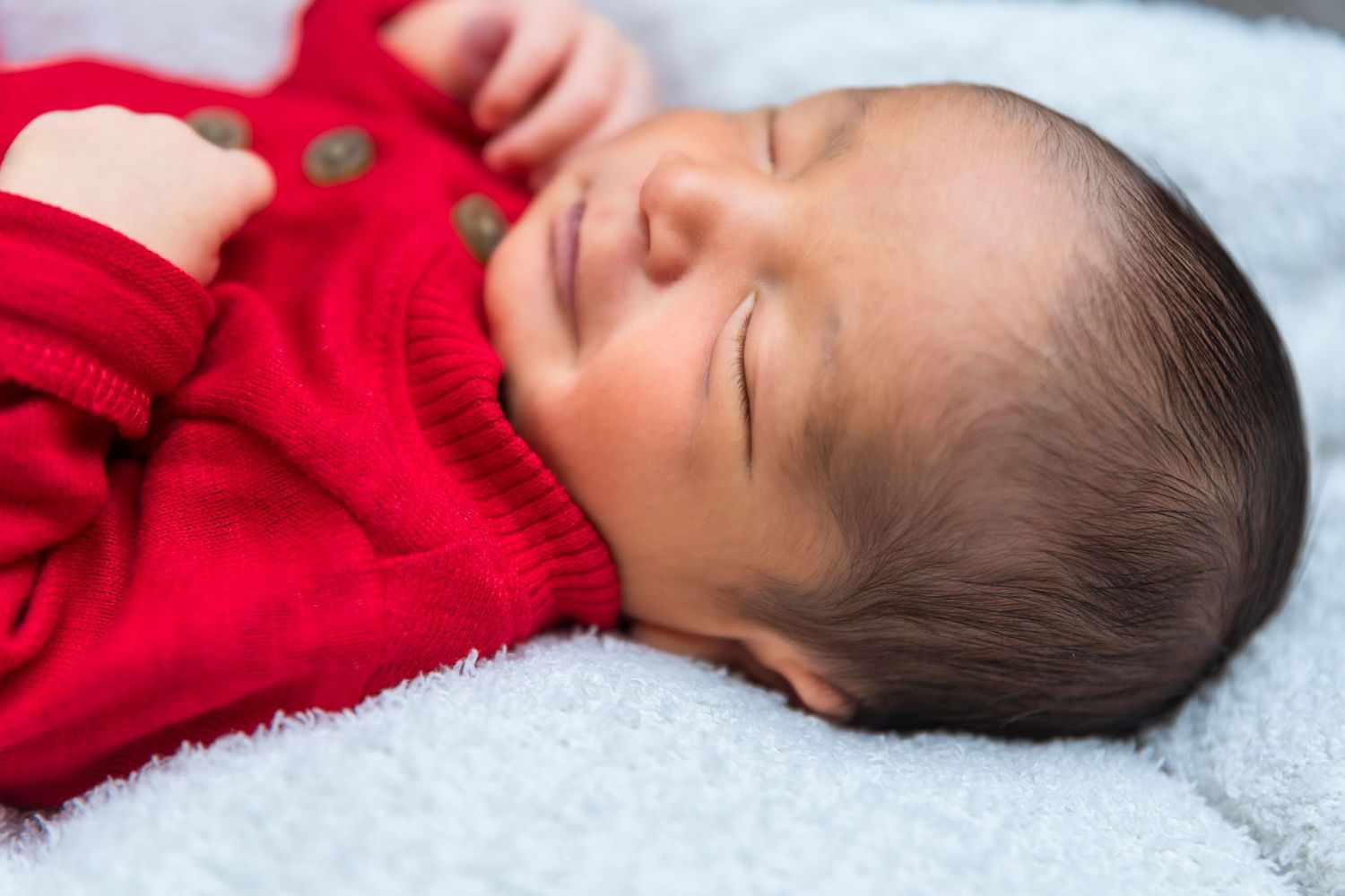 Baby in red sweater sleeping peacefully on white blanket.