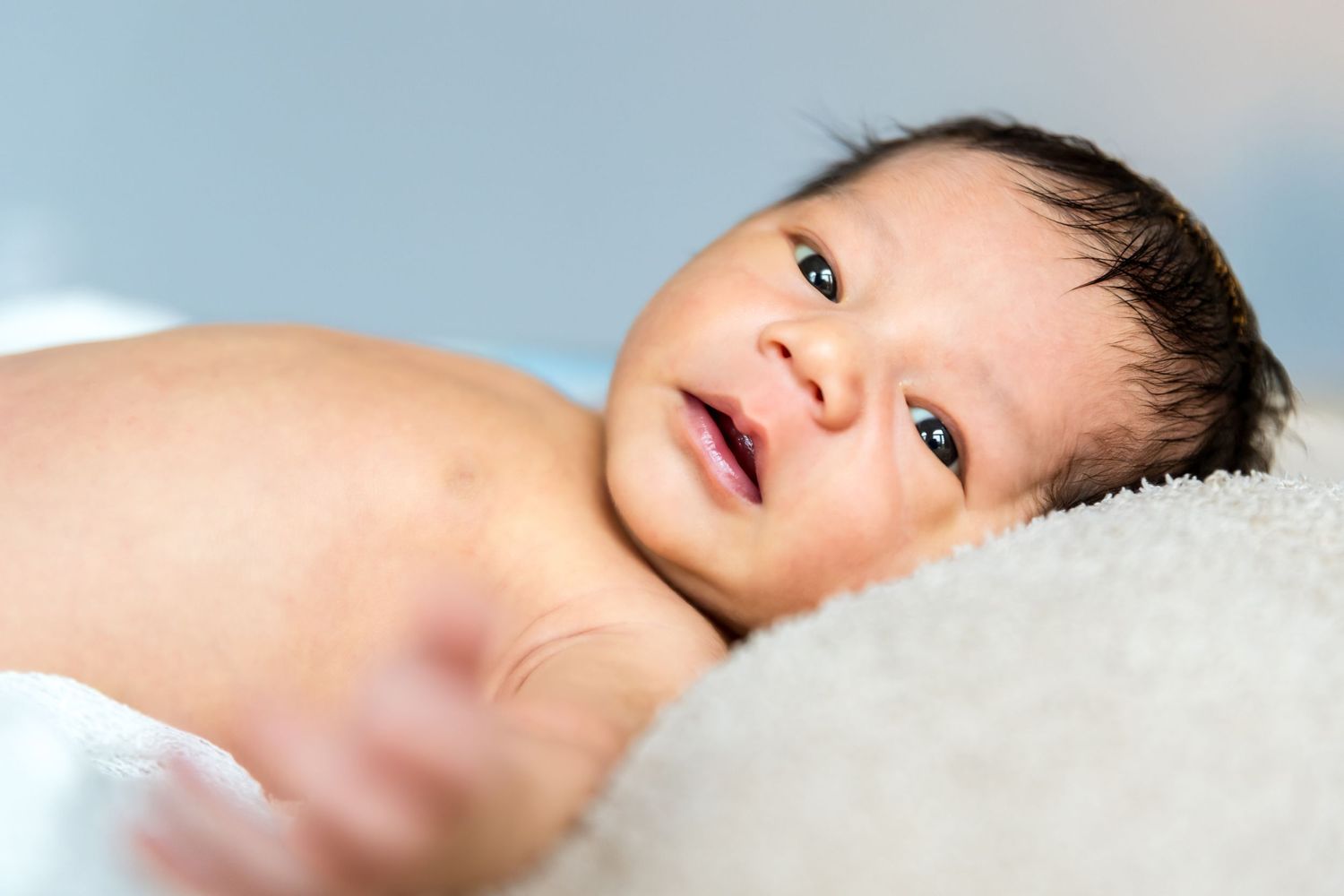 Close up of a baby lying on soft white blanket with bright eyes and peaceful expression.