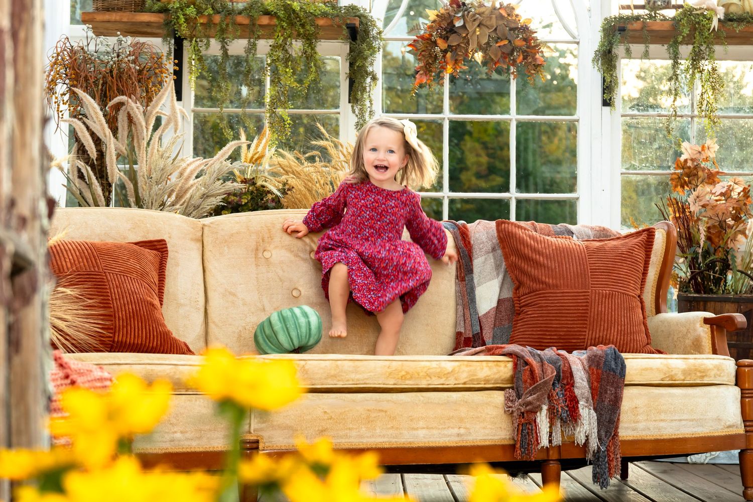 Cozy sunlit indoor seating area with yellow flowers and comfortable cushioned furniture.