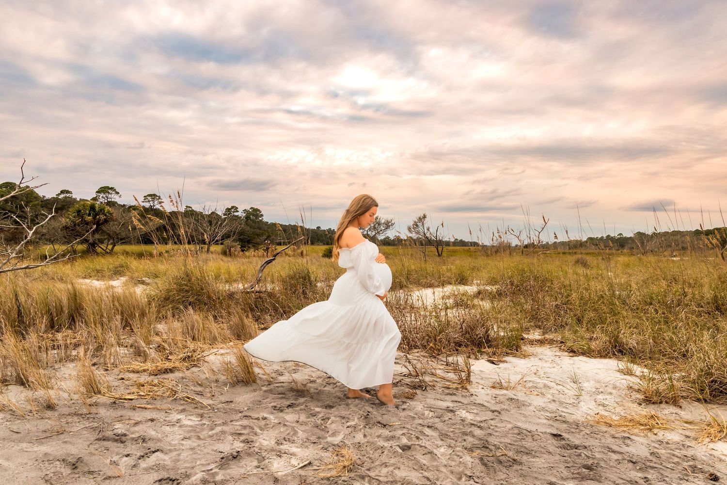 Wedding couple poses in golden light on sandy beach with flowing white dress.