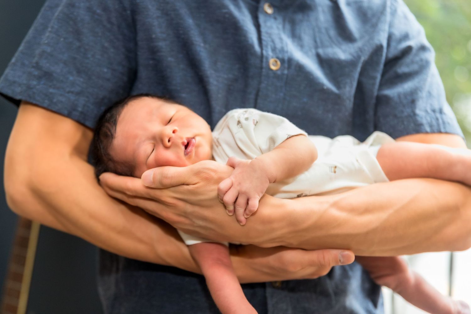 Gentle hands holding a sleeping newborn against blue clothing.