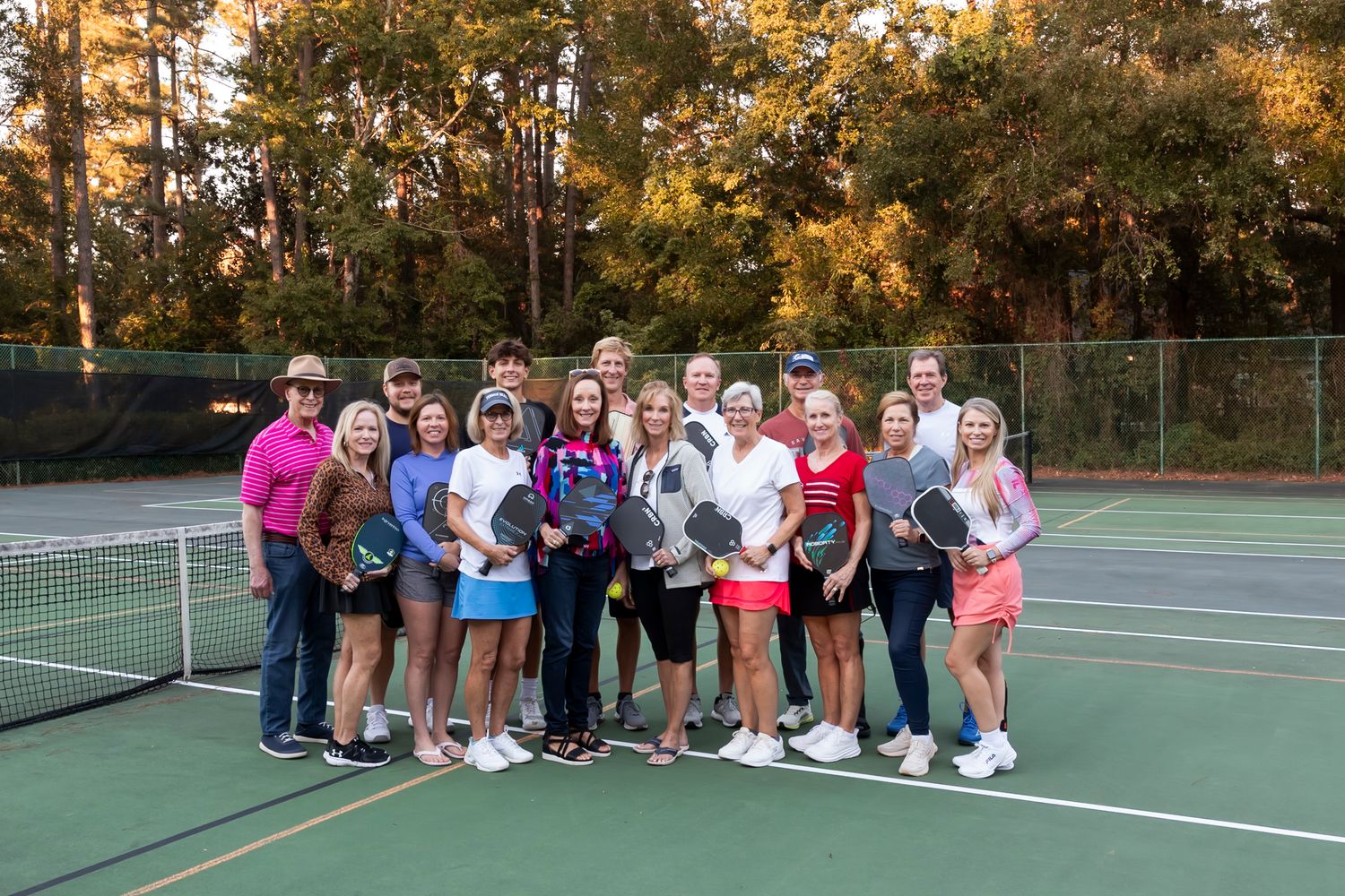 Group photo of tennis players gathered on outdoor courts during autumn.