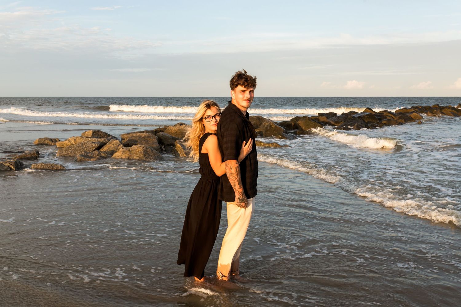 A romantic beach scene at sunset with waves crashing on rocky shore.