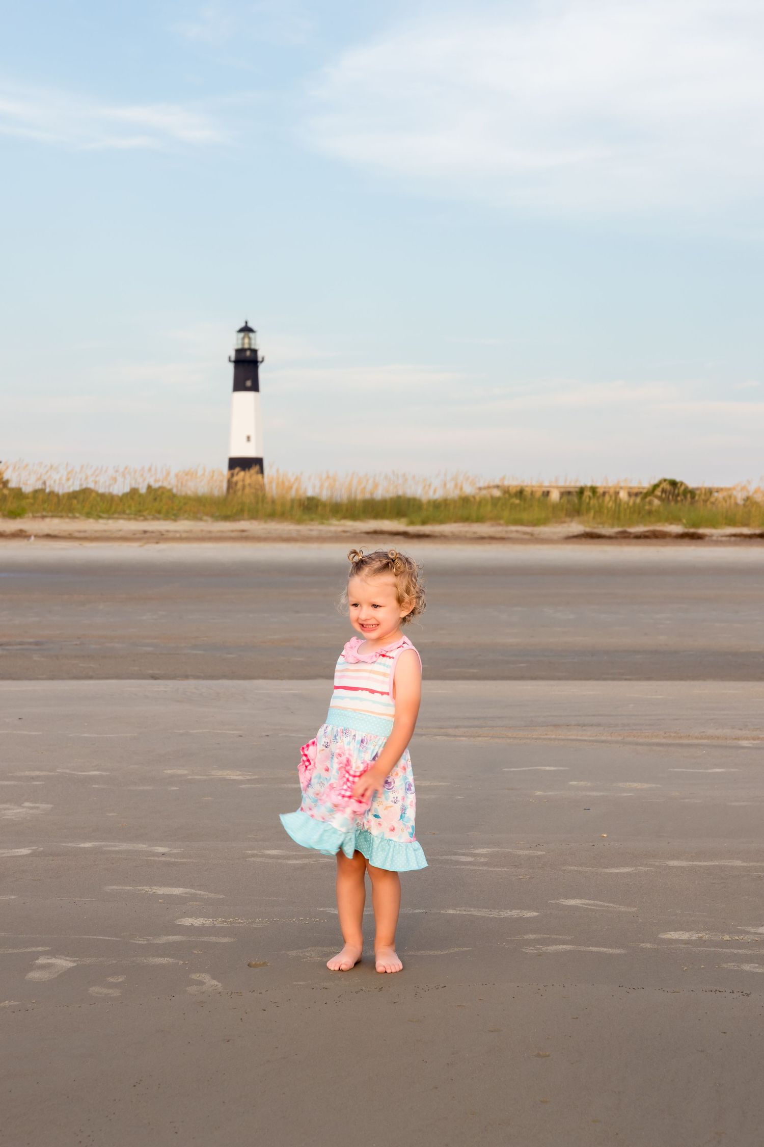 Small child plays on empty beach with lighthouse in background.