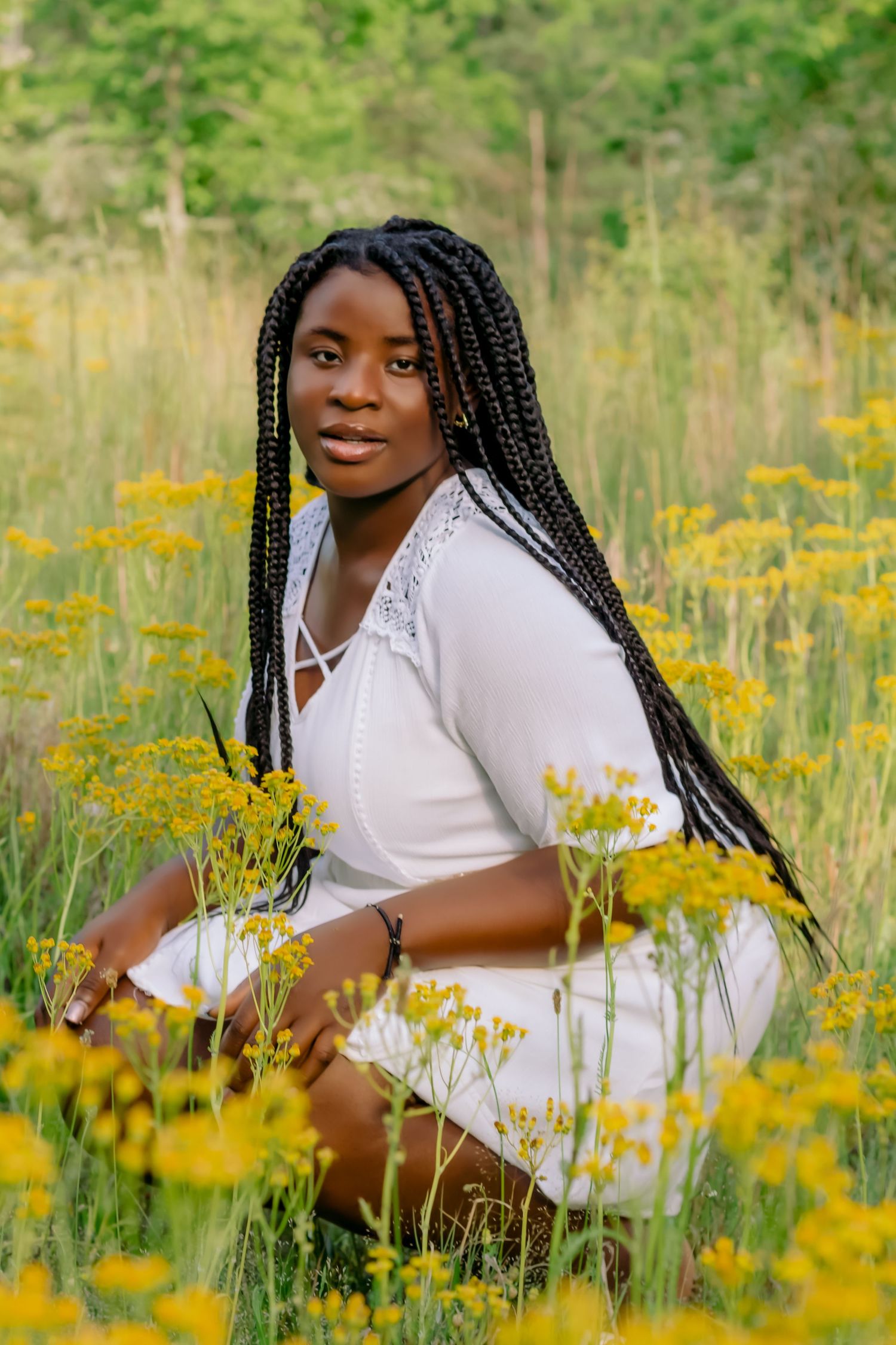 Person in white dress sitting among vibrant yellow wildflowers in a meadow.
