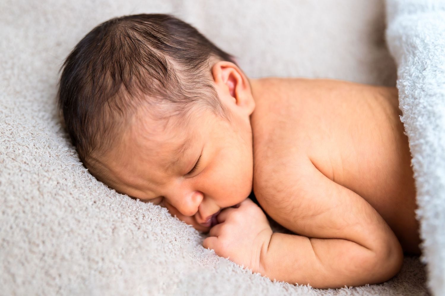 A sleeping newborn baby lies peacefully on soft white bedding in a series of connected photos.