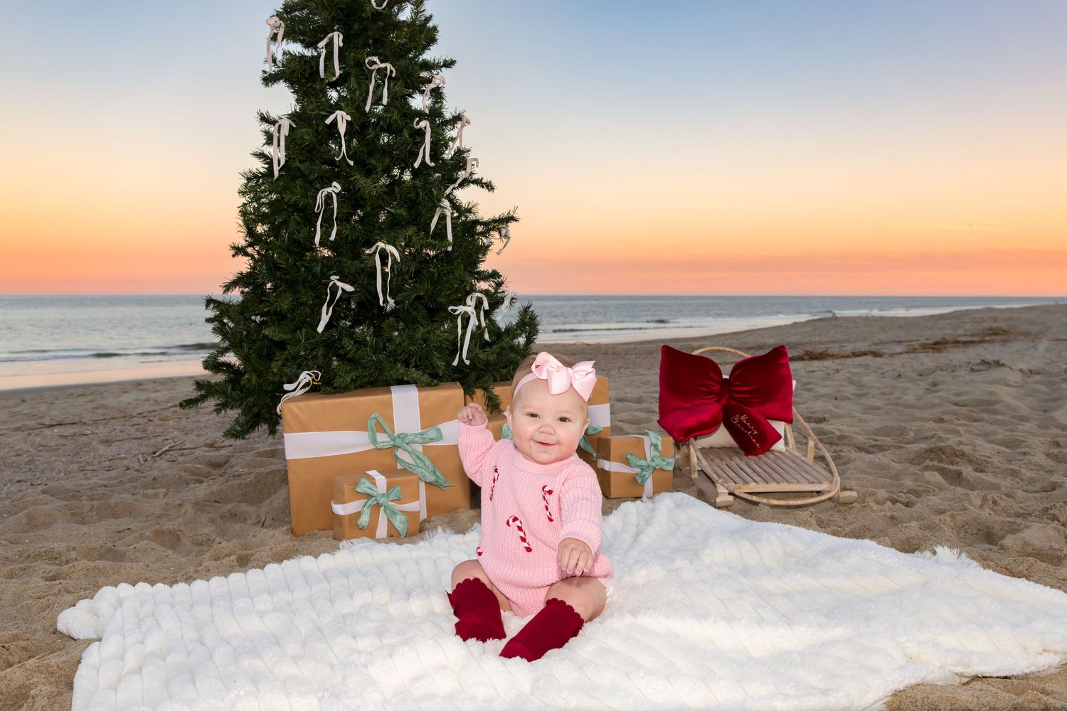 A Christmas tree decorated with ornaments stands on a sandy beach at sunset creating a festive coastal scene.