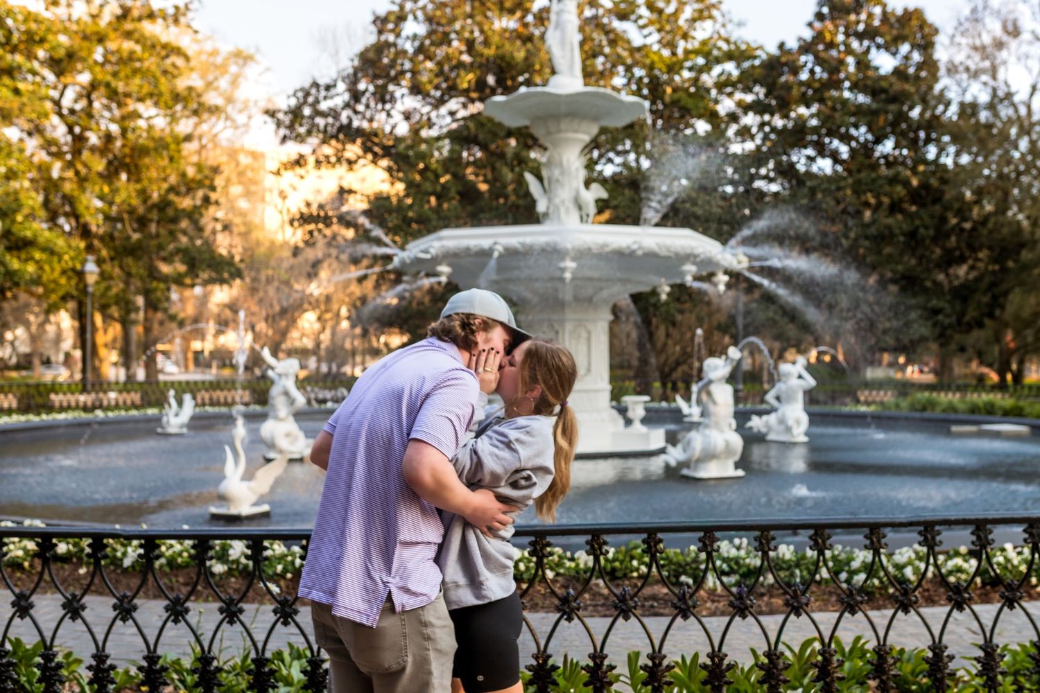 Romantic moment by an ornate white fountain in a park at sunset.