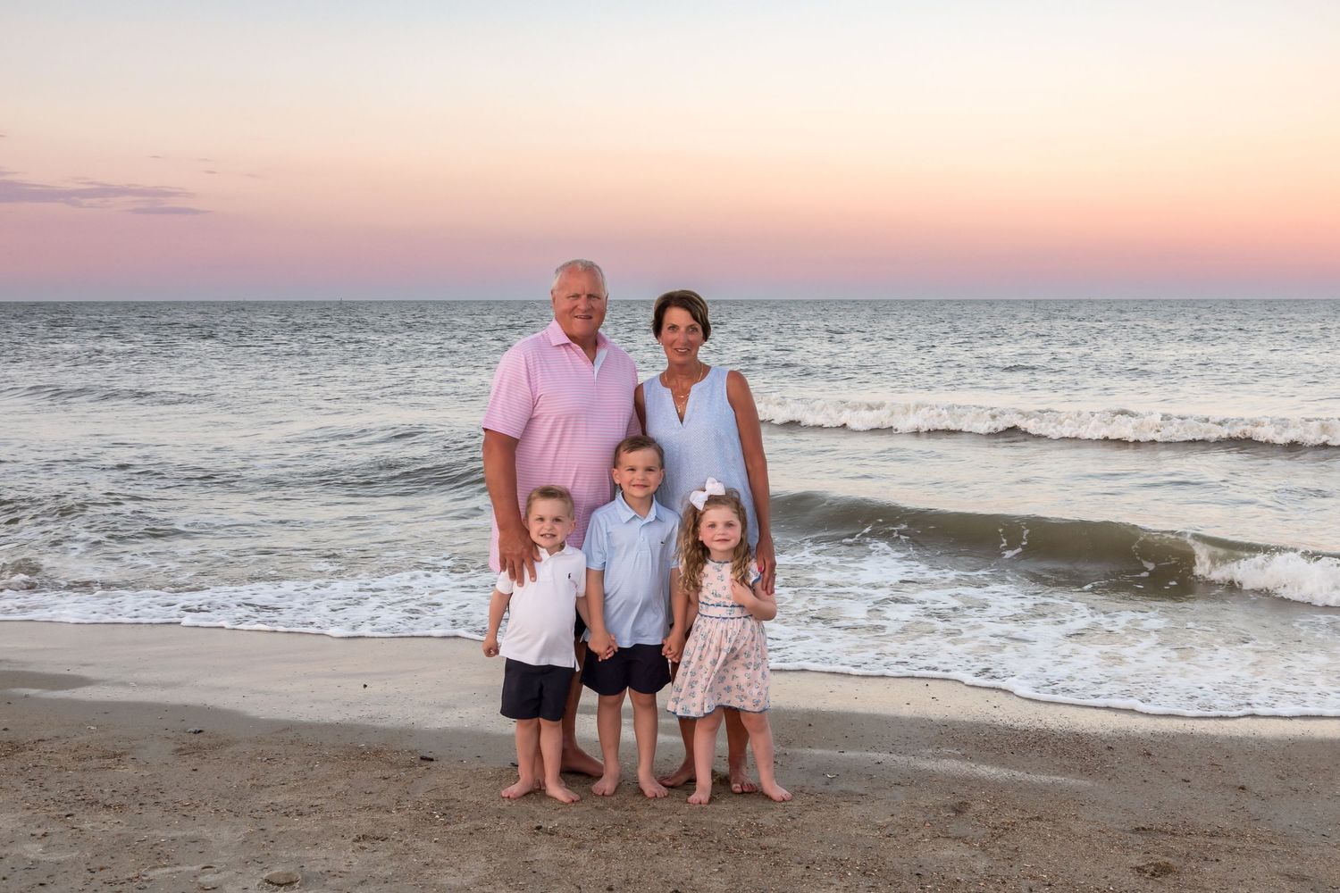 Family of five posing on beach at sunset with ocean waves behind them.