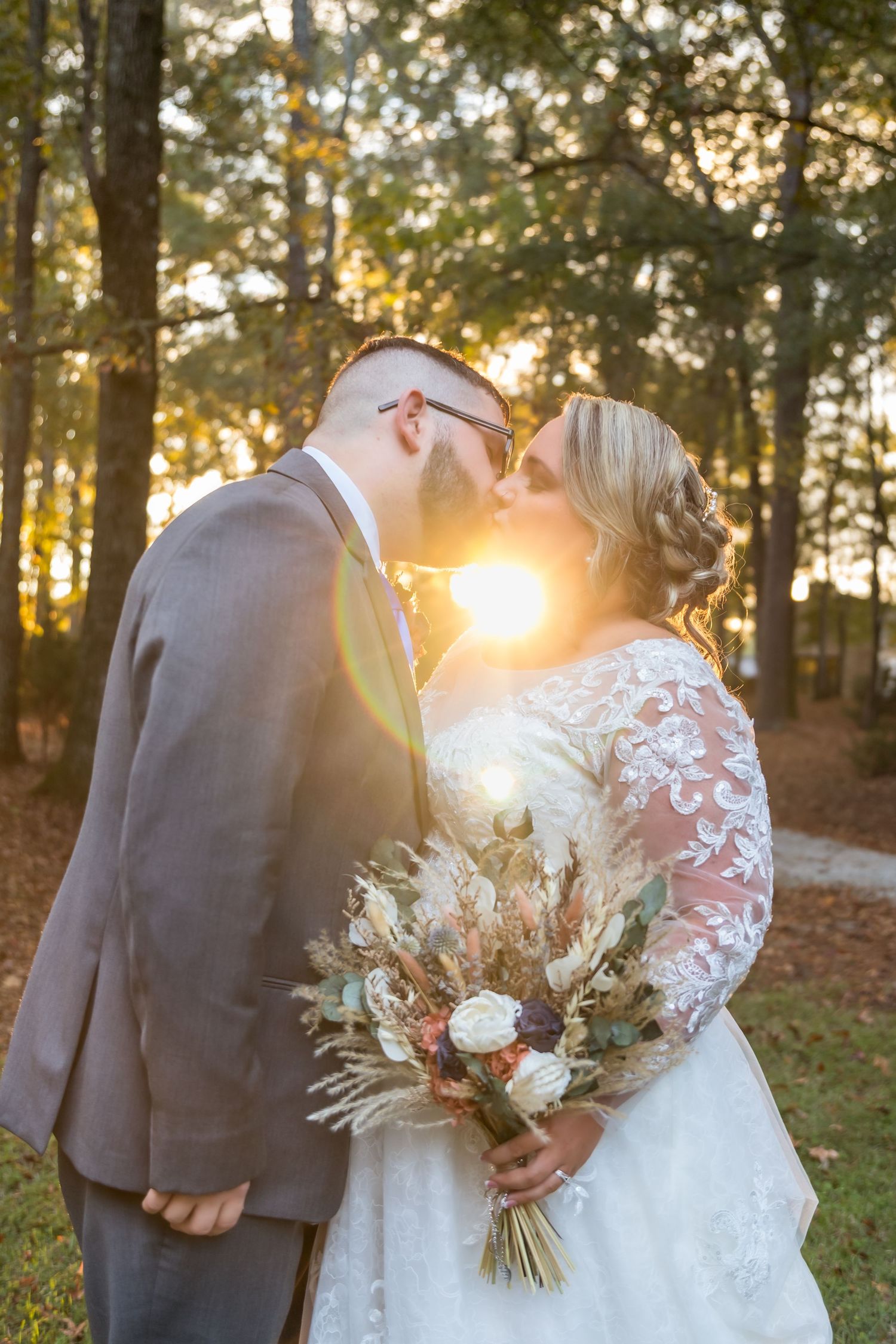 Romantic sunset wedding portrait with dried flower bouquet against forest backdrop.