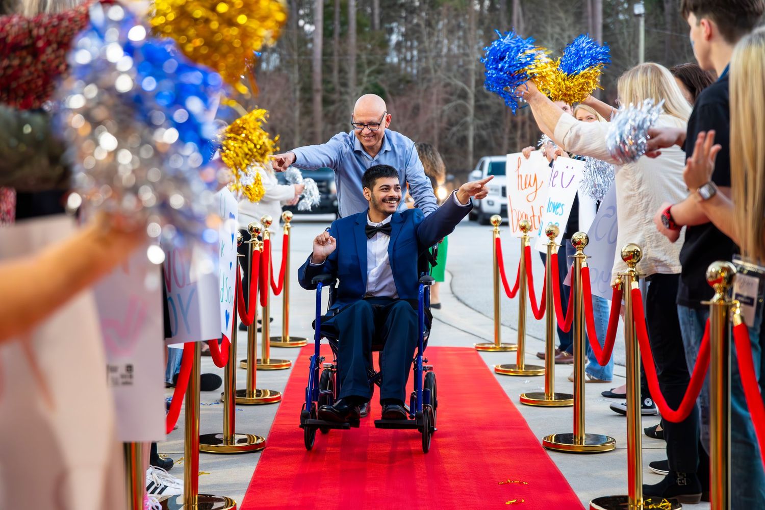 Outdoor red carpet walkway decorated with gold and blue balloons and rope barriers.
