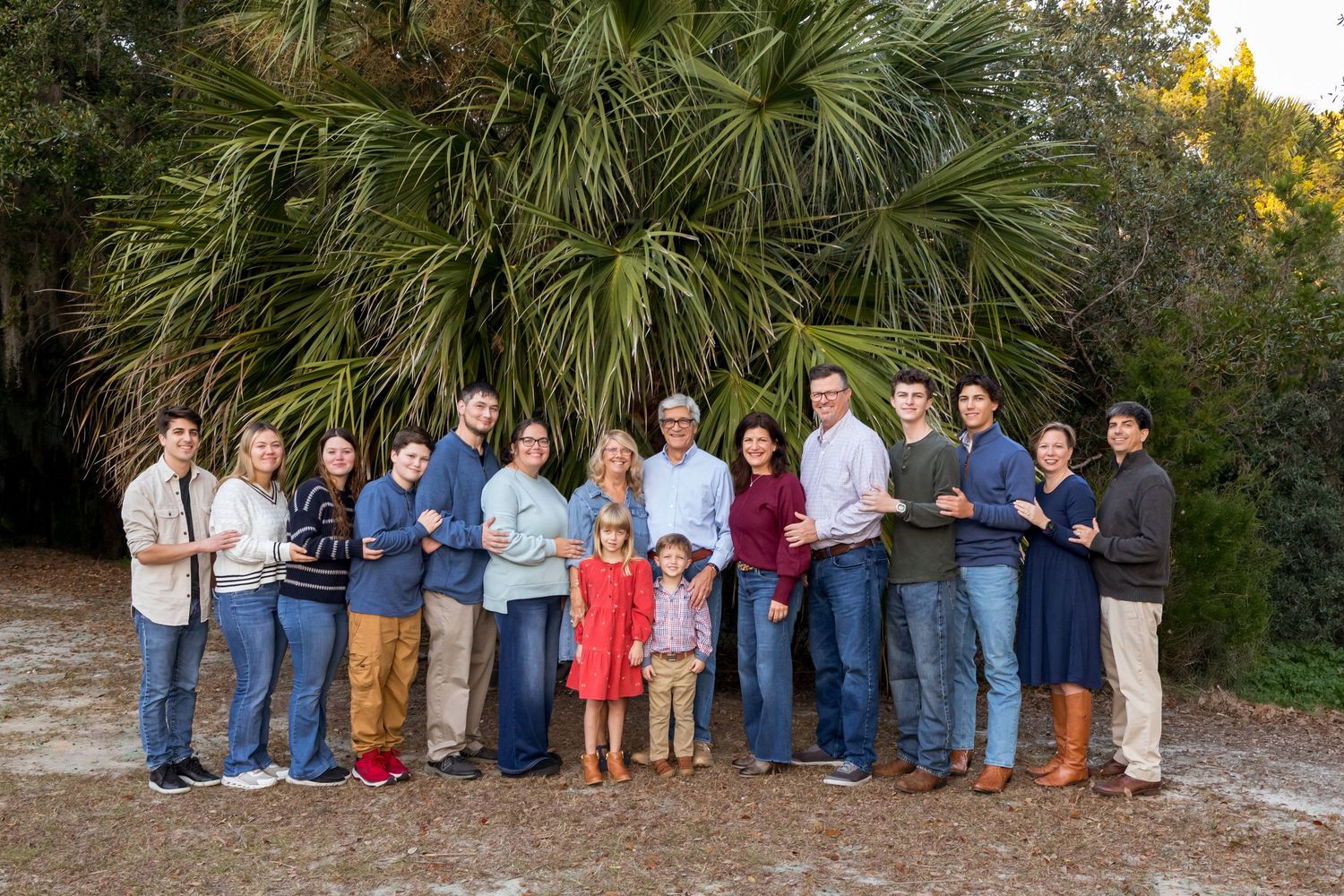 Large group photo of extended family gathered outdoors among palm trees and greenery.