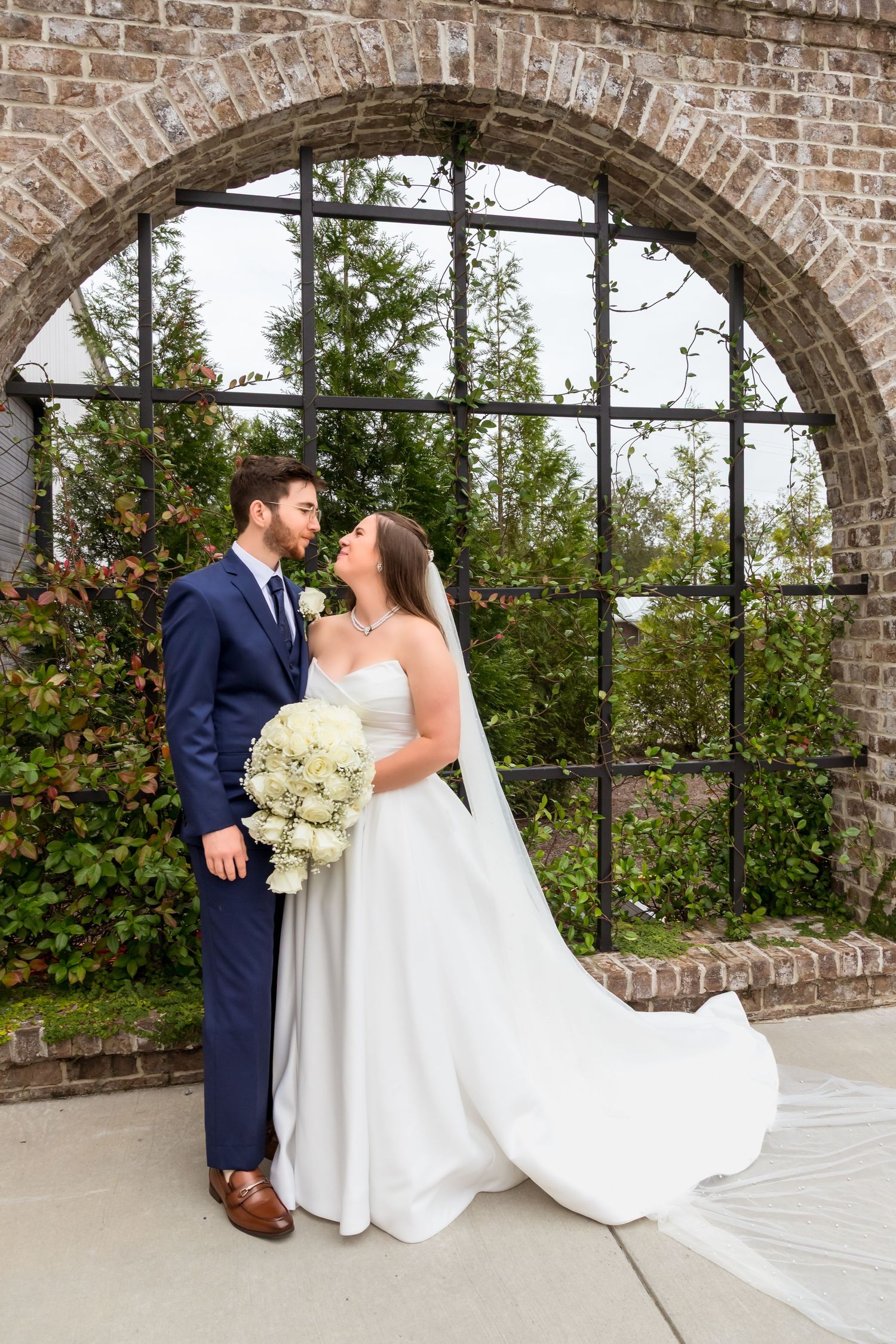 Wedding couple shares intimate moment under brick archway surrounded by greenery.