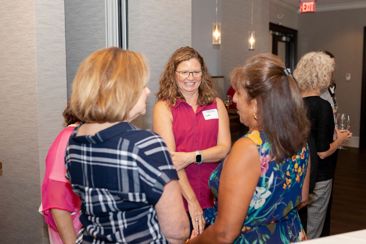 People mingling at an indoor social gathering with pendant lights hanging from the ceiling.