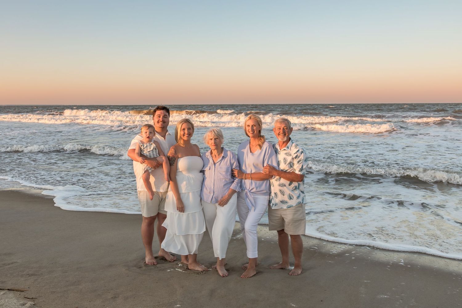 Group of women posing together on a sandy beach at sunset with ocean waves in the background.