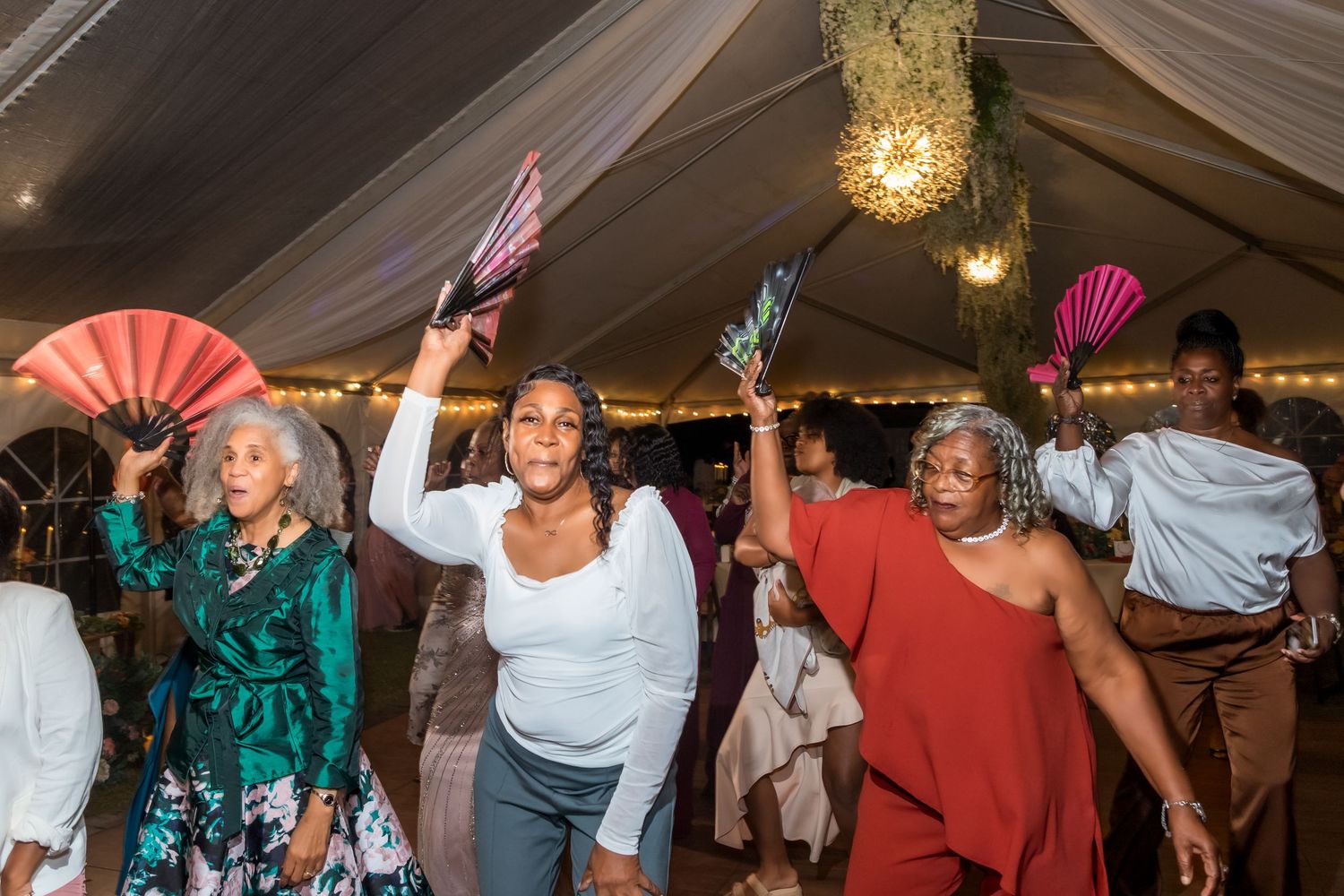 Wedding reception dance party with guests celebrating under draped tent lighting.