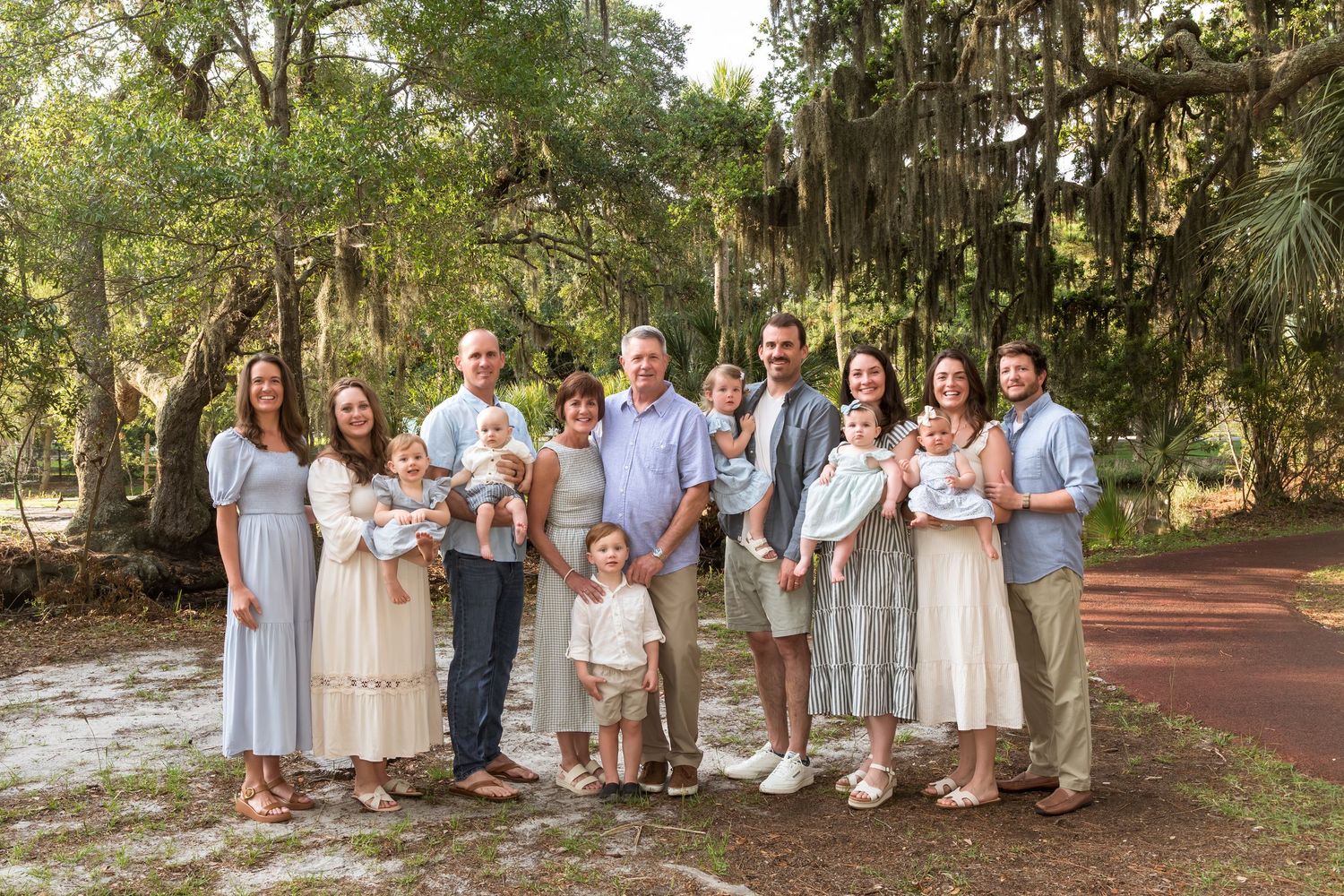 Large family group portrait outdoors among moss-covered trees, dressed in coordinating blue and white outfits.