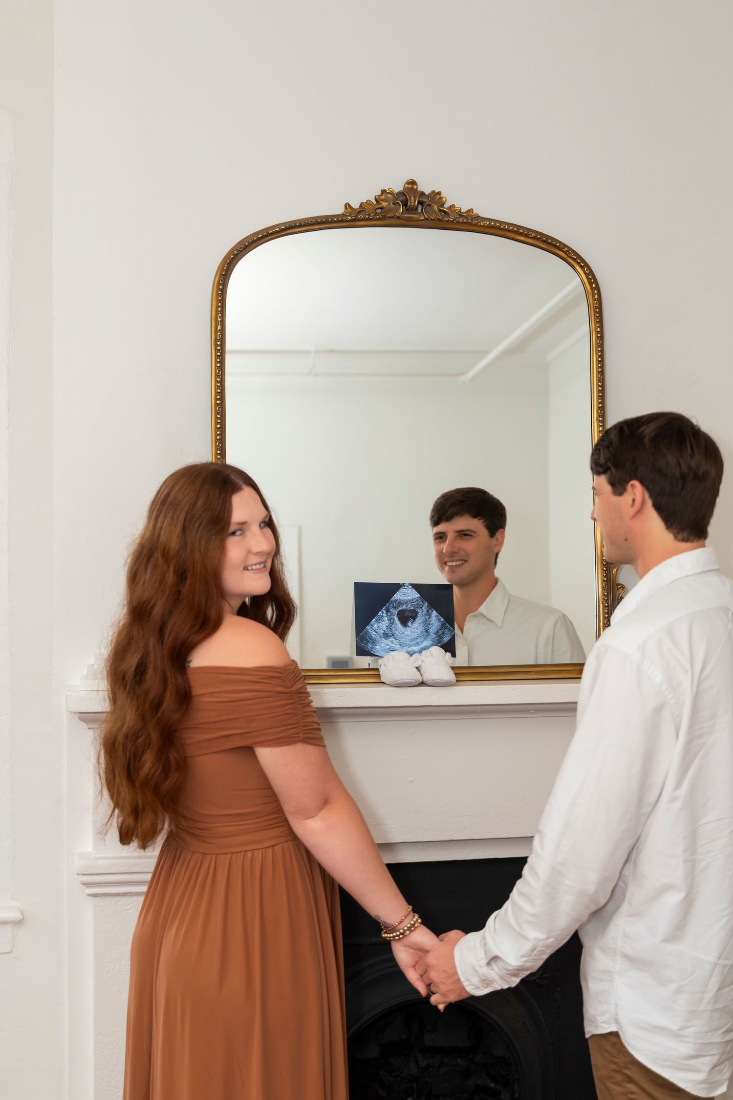 Couple looking at ultrasound photo reflected in ornate gold mirror.