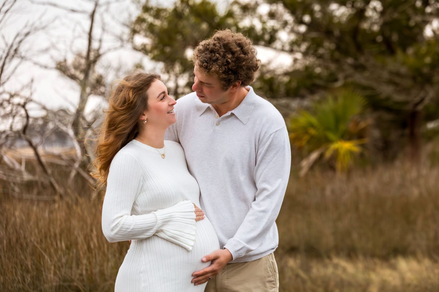A couple in white and neutral outfits share romantic moments in a rustic outdoor setting during their engagement session.