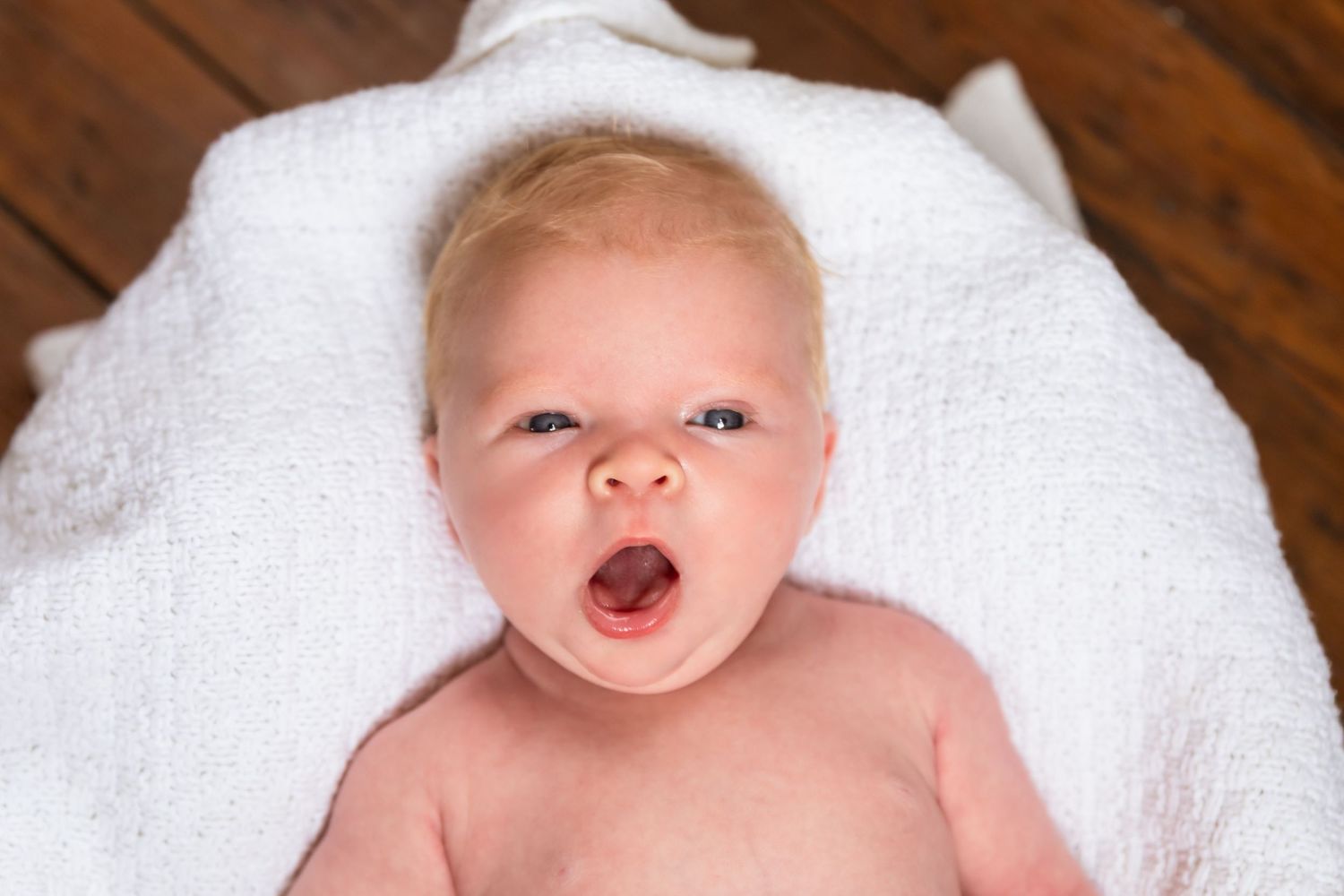 A series of five photos showing a baby in white blankets making different facial expressions.