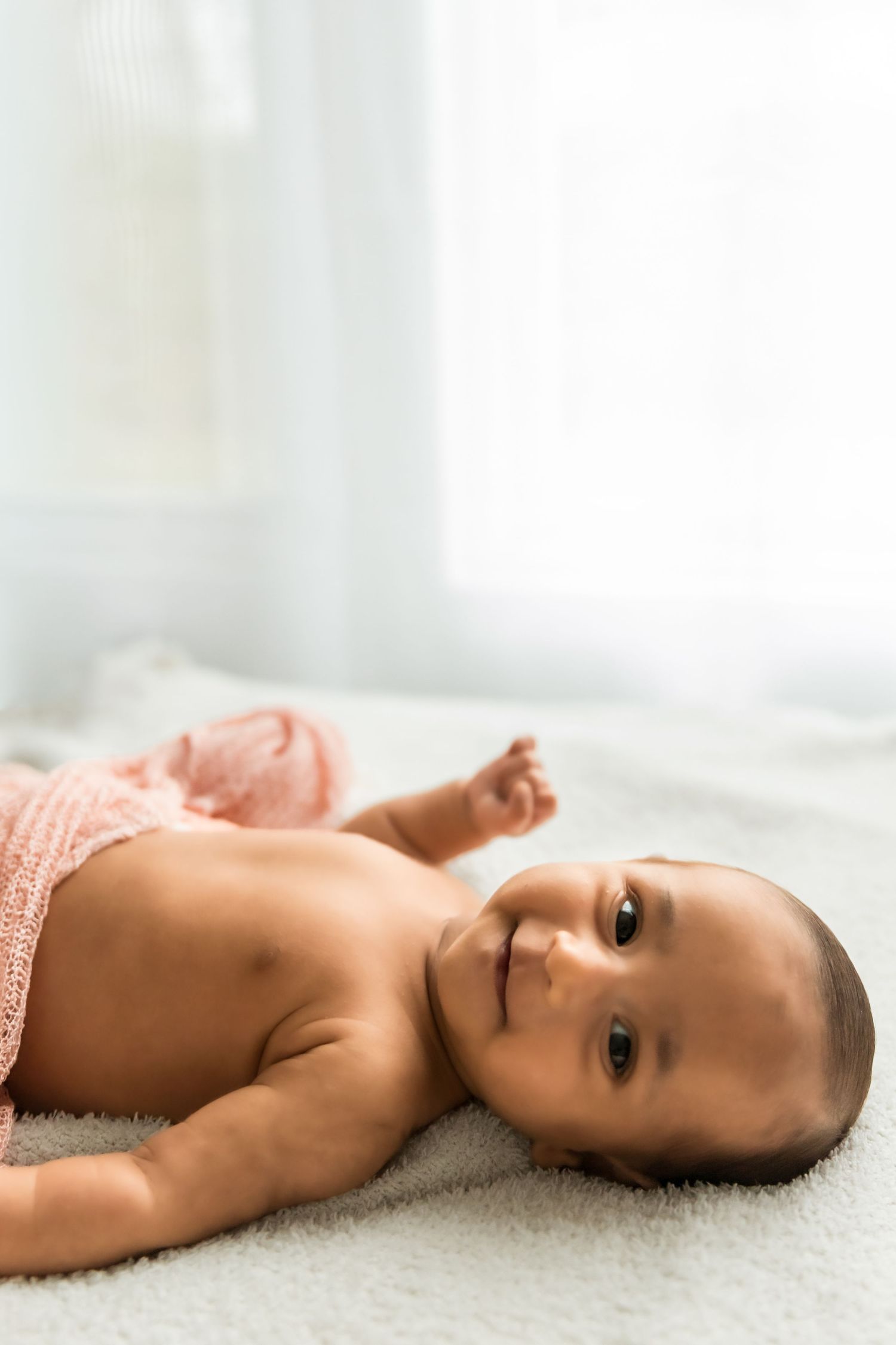 Baby resting on soft white carpet in natural light setting.