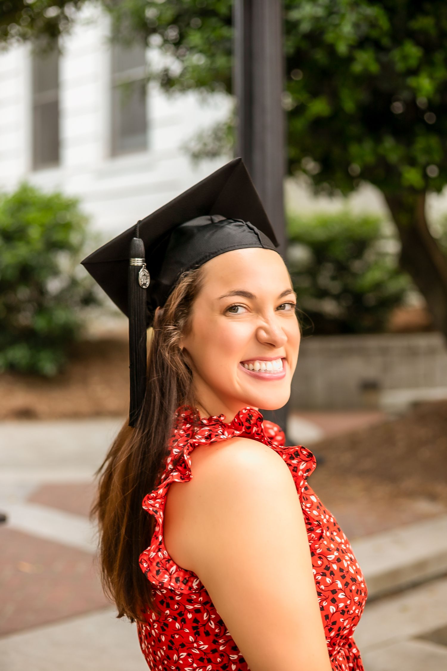 Graduate in cap posing in a red polka dot dress near campus buildings.